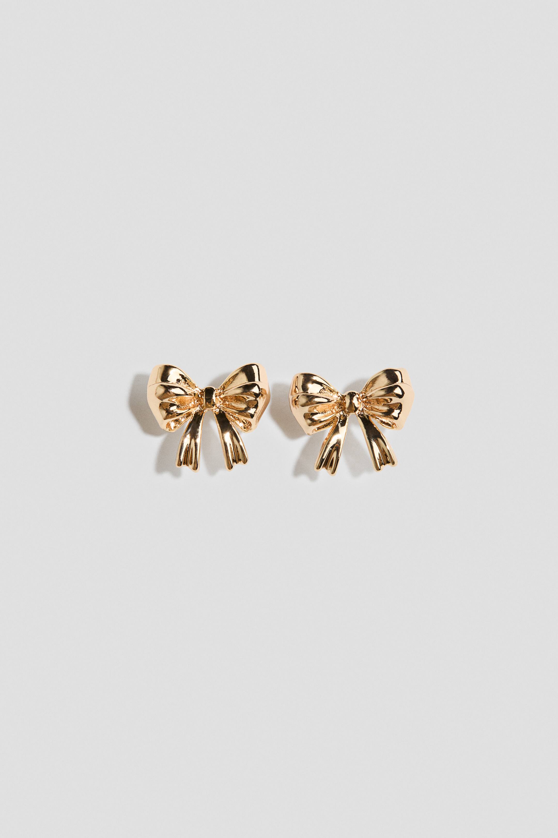 View larger image: A pair of gold-tone bow earrings is shown from the front, featuring a polished metallic finish with a sculpted bow design and two draped ribbon tails.