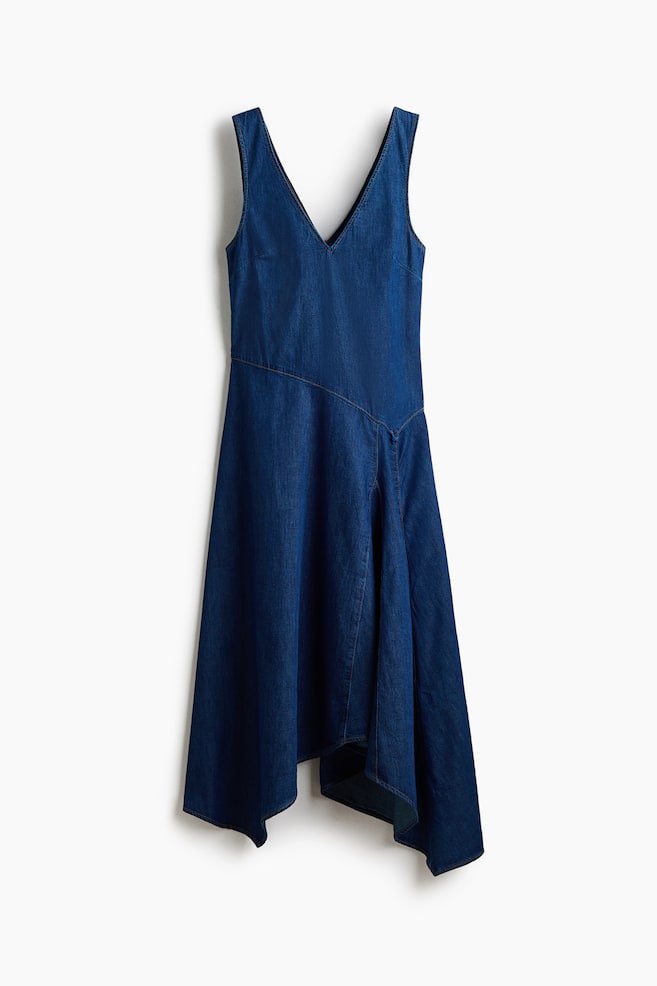 A blue denim dress is hanging flat, facing front, featuring a V-neckline and a sleeveless design. It is detailed with a diagonal seam across the body and an asymmetric hemline with a flared skirt. - 1