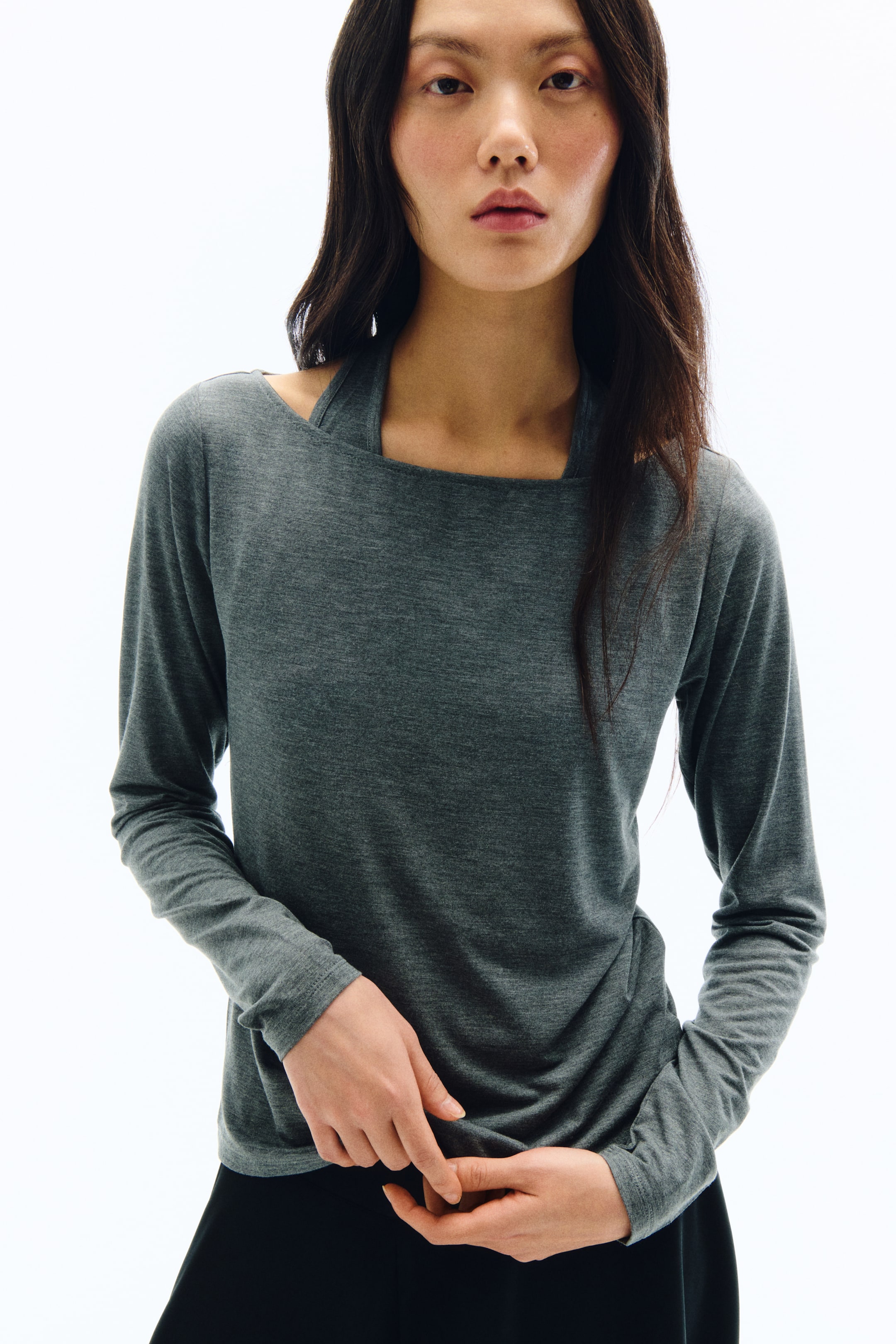 拡大画像を表示: 杢調のダークグレーの長袖トップスがフロントと左側から写されており、スクエアネックラインに一体型のホルタースタイルストラップがあしらわれたデザインが特徴です。袖は手首までのロングスリーブで、身頃部分の生地はゆったりとしたドレープ感をもって落ち感のあるシルエットを描いています。