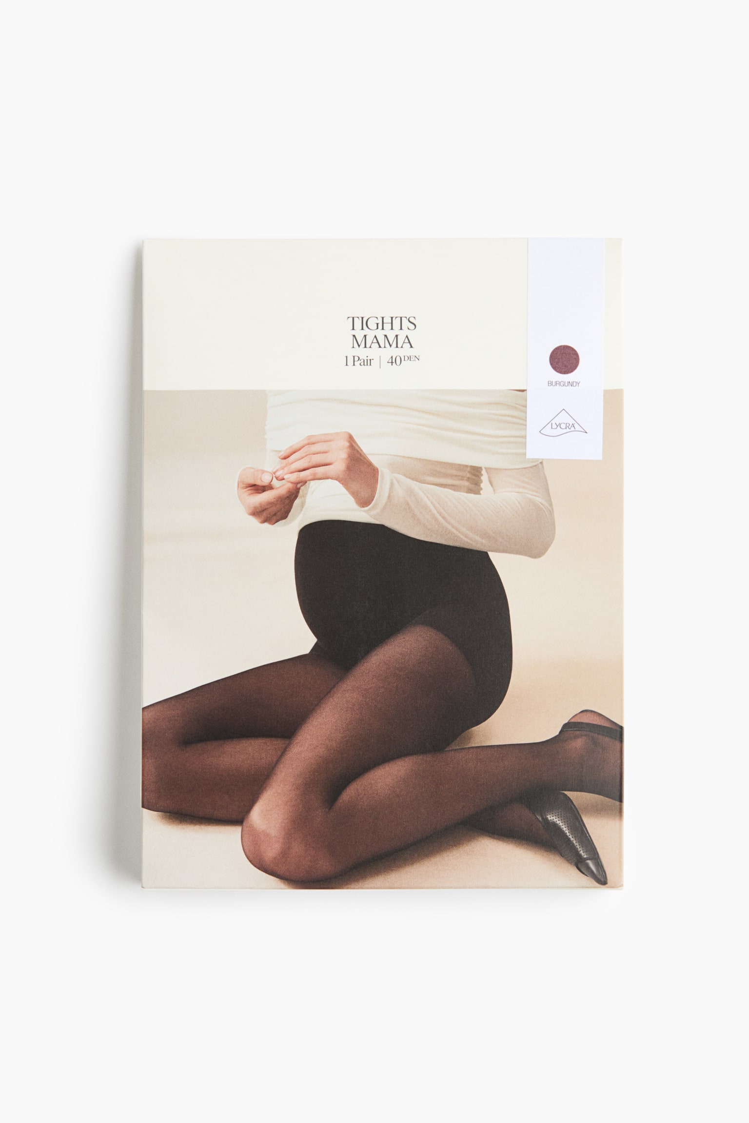 Pravougaona kutija za pakovanje âTights Mamaâ trudniÄkih Äarapa okrenuta je ka prednjoj strani i ima kremasti gornji deo sa nazivom proizvoda âTIGHTS MAMA, 1 Pair \| 40 DENâ i uspravnu belu oznaku na desnoj strani koja ukazuje na bordo boju. Donji deo pakovanja prikazuje fotografiju trudne modela kako sedi na podu i nosi providne bordo Äarape, stilizovane uz belu bluzu dugih rukava spuÅ¡tenih ramena i crne slingback ravne cipele.