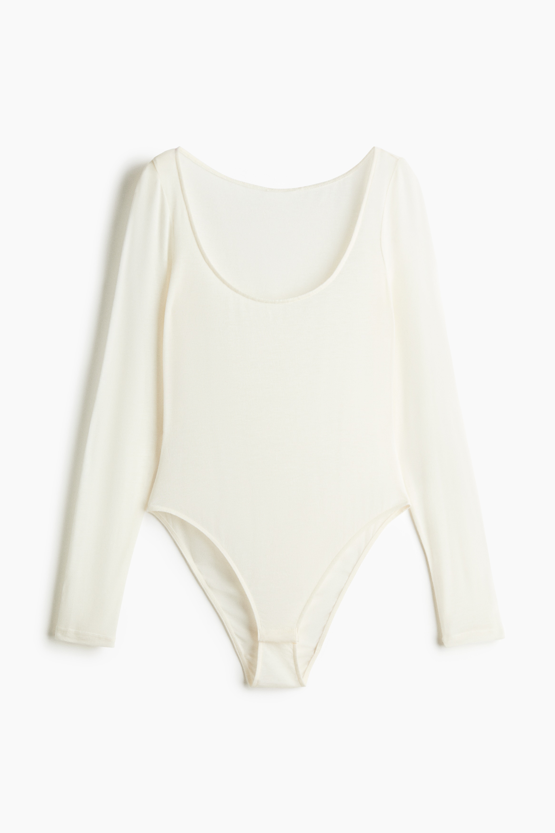 En lÃ¥ngÃ¤rmad body i benvitt mjukt jerseymaterial bÃ¤rs av modellen. Bodyn har en rundad urringning och Ã¤r stylad med matchande benvita ribbade strumpor.