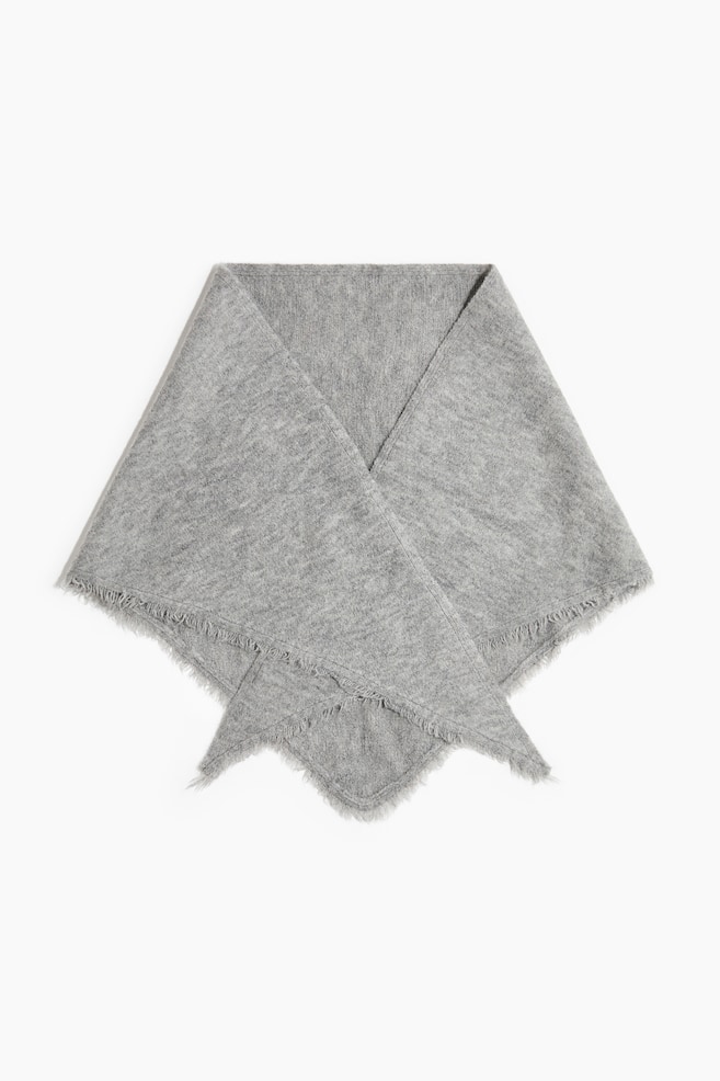 Une Ã©charpe triangulaire en maille chinÃ©e gris clair est posÃ©e Ã  plat, vue de face, pliÃ©e symÃ©triquement avec ses extrÃ©mitÃ©s pointues qui se chevauchent en bas. LâÃ©charpe prÃ©sente un tissage doux et texturÃ©, ainsi quâune dÃ©licate frange effilochÃ©e le long de tous les bords visibles. - 1