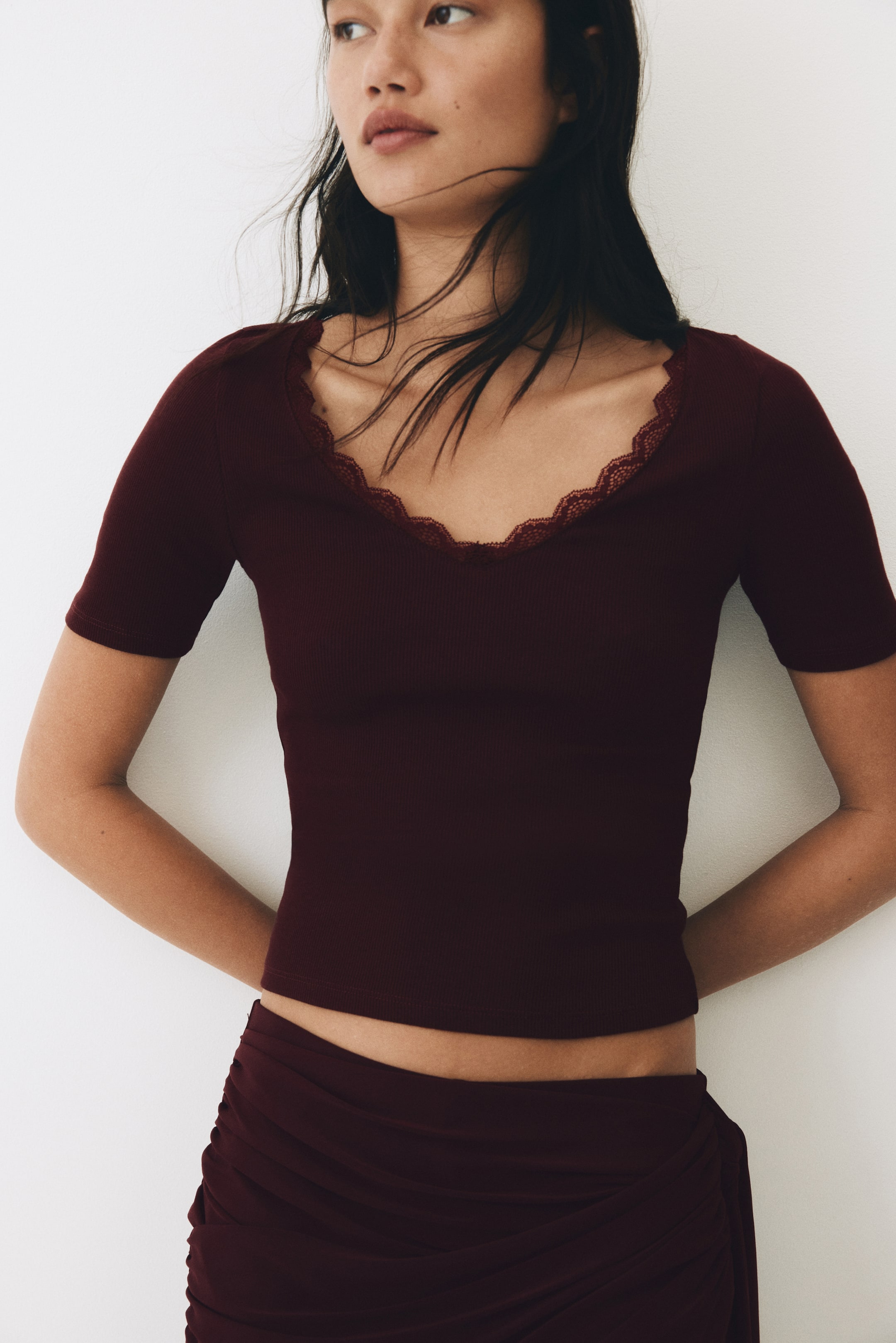 Zobacz większy obraz: Ciemnoczerwona prążkowana bluzka z krótkim rękawem, z dekoltem w łódkę ozdobionym delikatną koronką, prezentująca dopasowaną sylwetkę i kończąca się na wysokości talii.