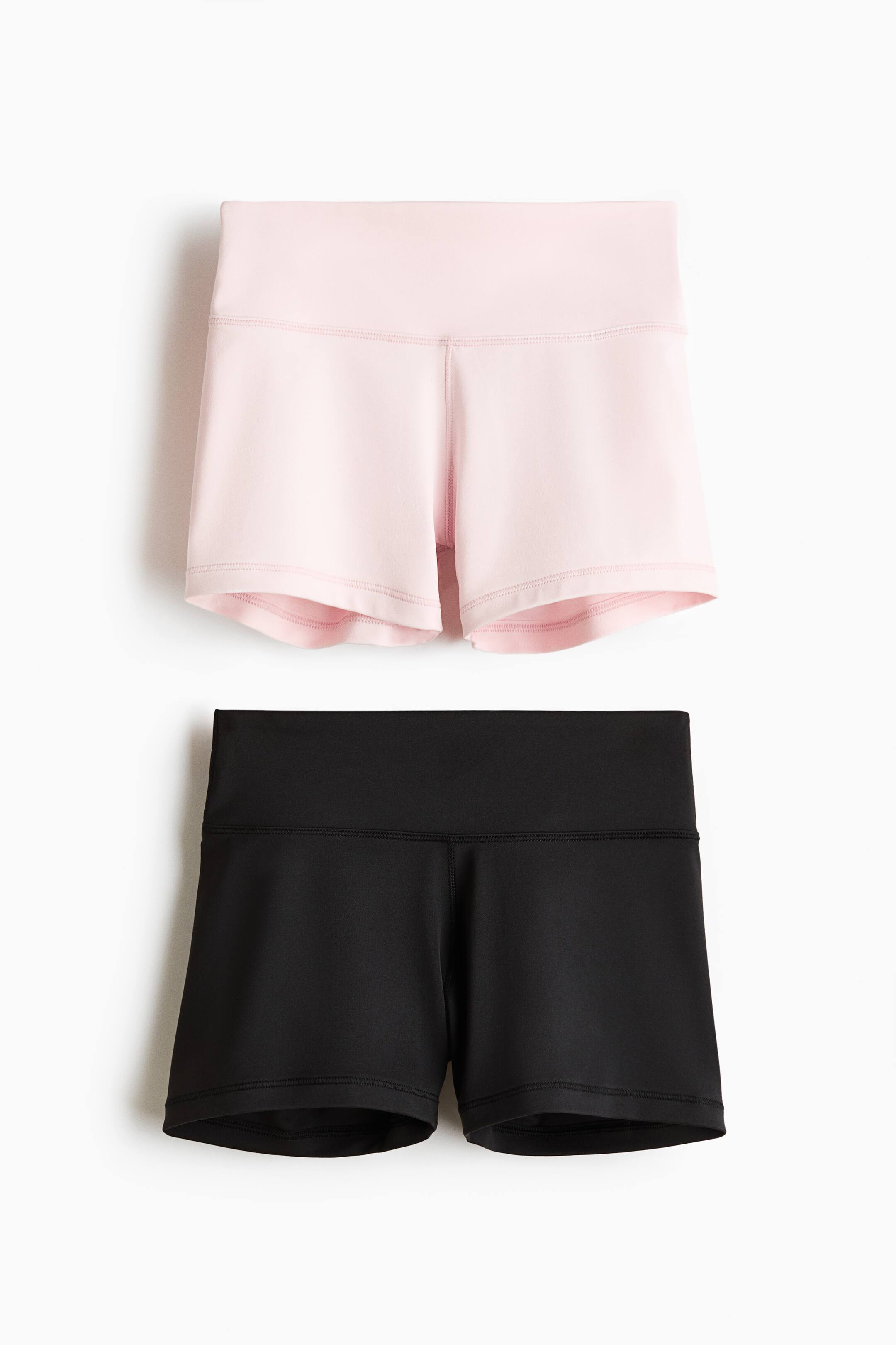 Grotere afbeelding bekijken: Een 2-pack korte sportfietsshorts toont een lichtroze en een zwarte variant, elk met een brede, hooggesneden tailleband en flatlocknaden. Beide shorts worden in vooraanzicht gepresenteerd.