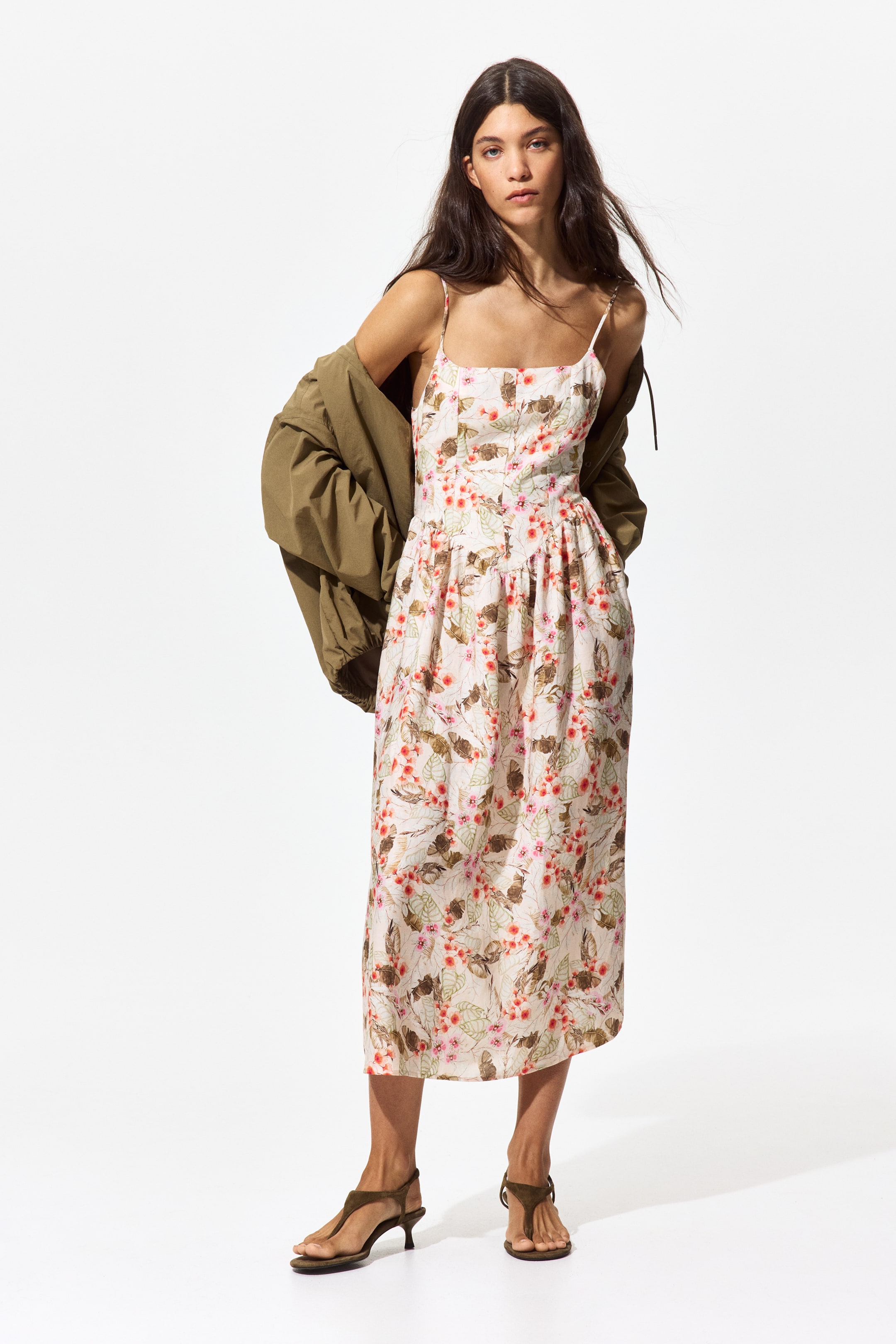 View larger image: A front-facing midi camisole dress showcases a floral pattern in pink and brown hues on a light backdrop. It is crafted with a square neckline, slender spaghetti straps, a button-front bodice, and a gathered waist leading to a flowing skirt, complemented by a khaki jacket draped over its shoulders.