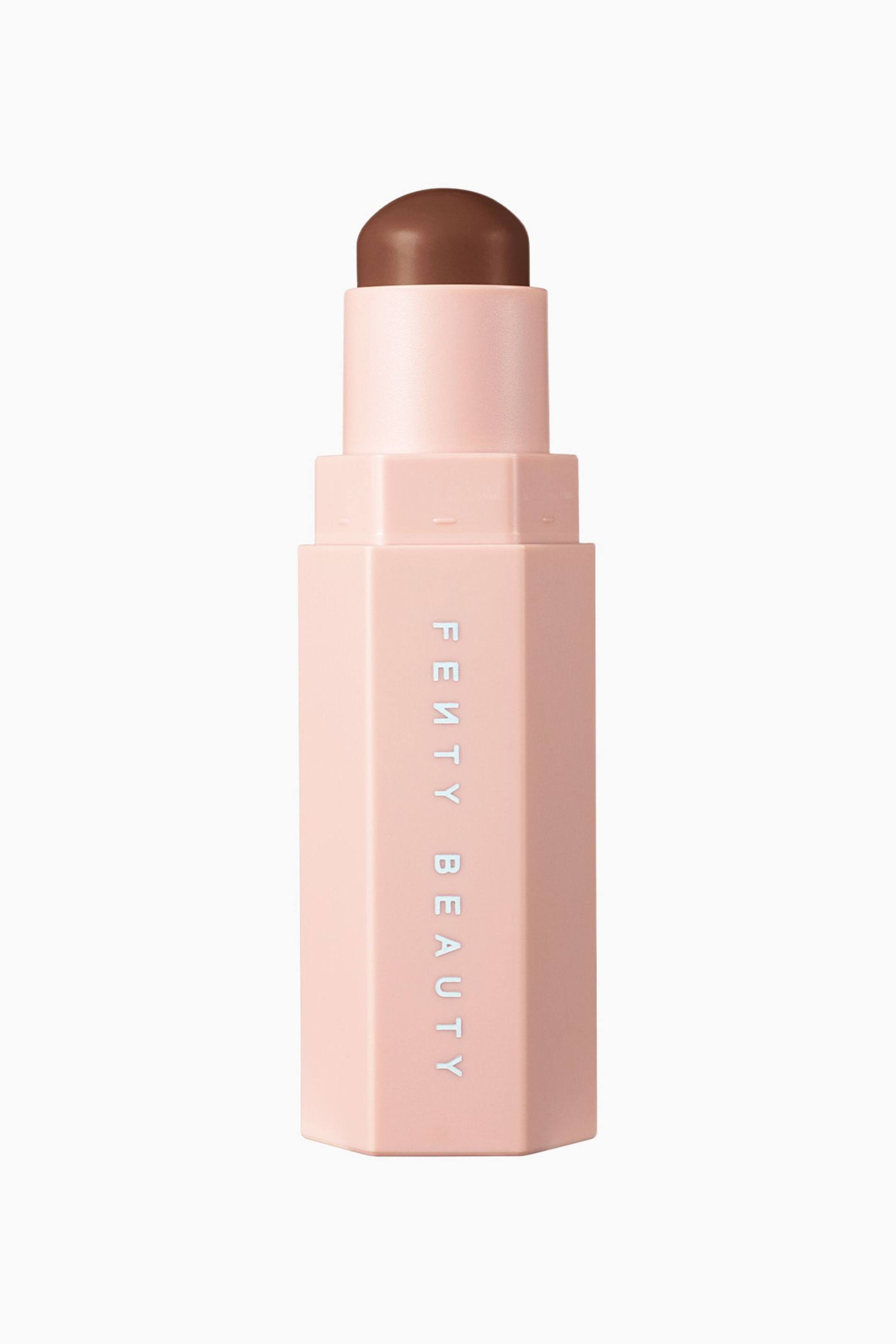 Näytä suurempi kuva: Vaaleanpunainen, kuusikulmainen contour-stick seisoo pystyasennossa, ja sen yläosasta on esillä kupolimainen, tummanruskea meikkivoide. Etupaneelissa mattapintaisessa kotelossa näkyy pystysuuntainen valkoinen "FENTY BEAUTY" -brändäys.