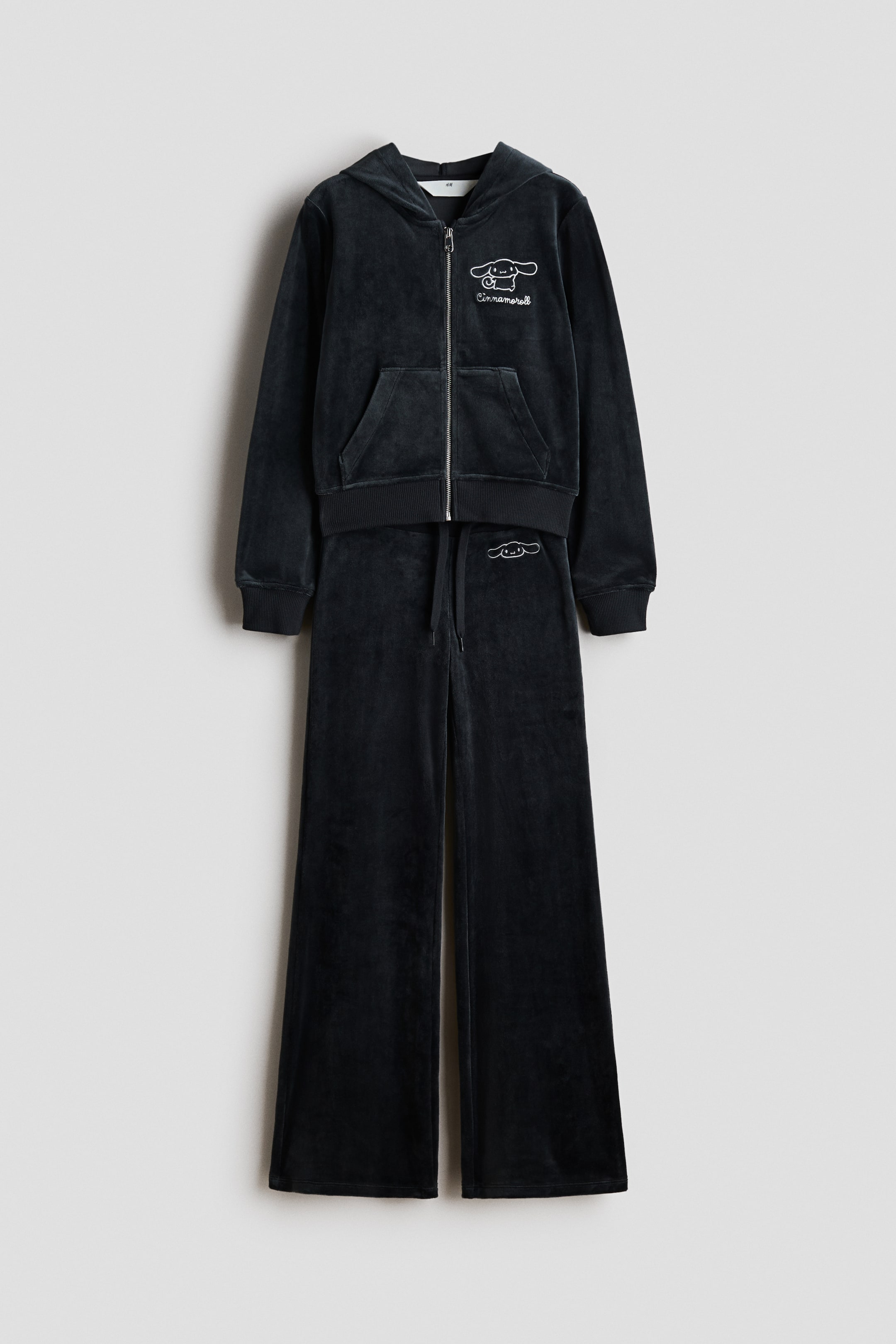 View larger image: Presenting a dark grey velour tracksuit, featuring a full-zip hoodie with a white embroidered Cinnamoroll character and text on the left chest, ribbed cuffs, a ribbed hem, and kangaroo pockets. The matching wide-leg pants come with a drawstring waist and a small embroidered Cinnamoroll character on the left hip.