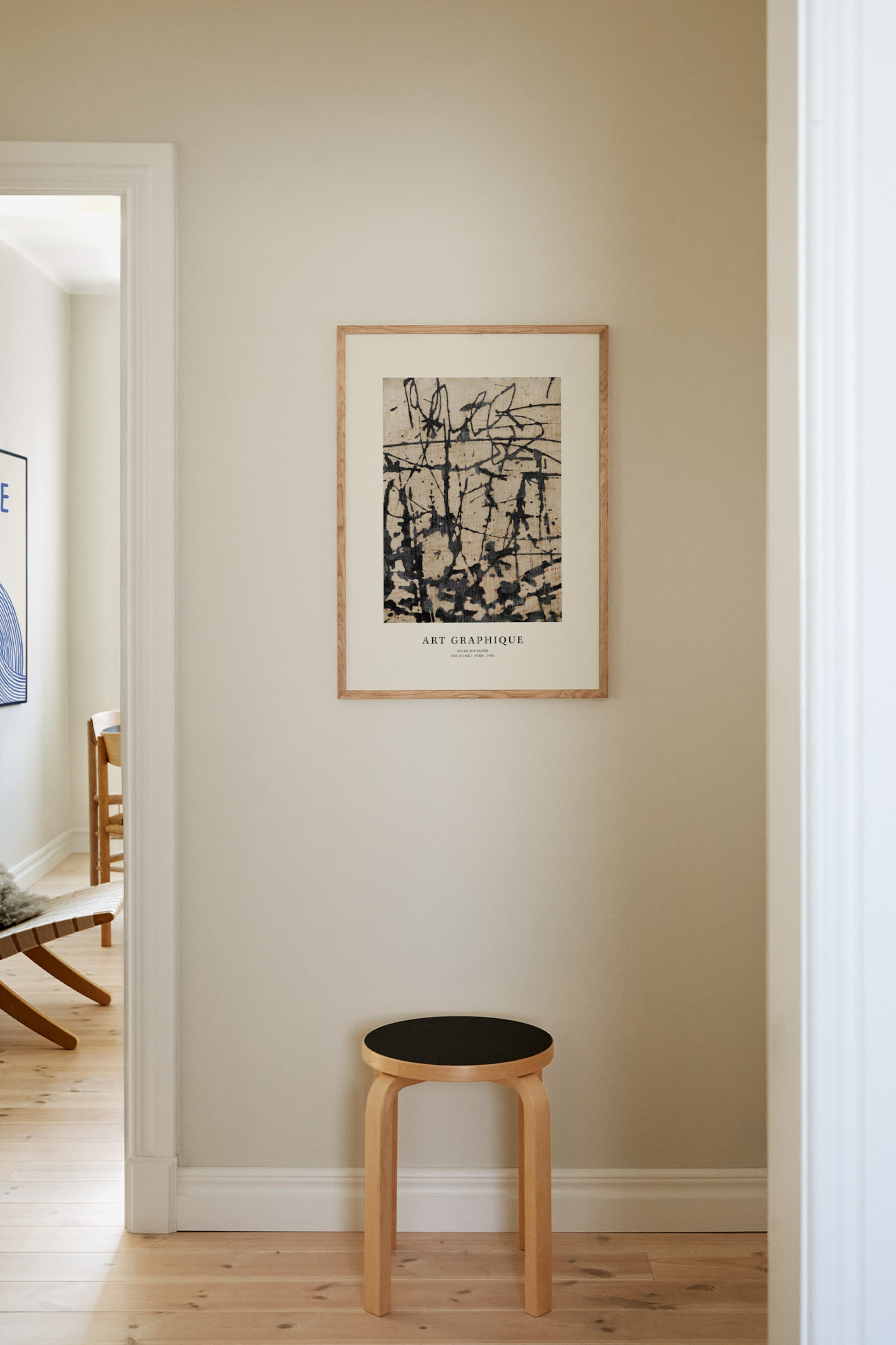 Grotere afbeelding bekijken: Een rechthoekige kunstdruk met zwarte abstracte spatten en lijnen op een lichtgekleurde, gestructureerde achtergrond, omlijst met lichtgekleurd hout. Het toont de tekst "ART GRAPHIQUE" en kleinere tekst onderaan, en is recht naar voren gericht.