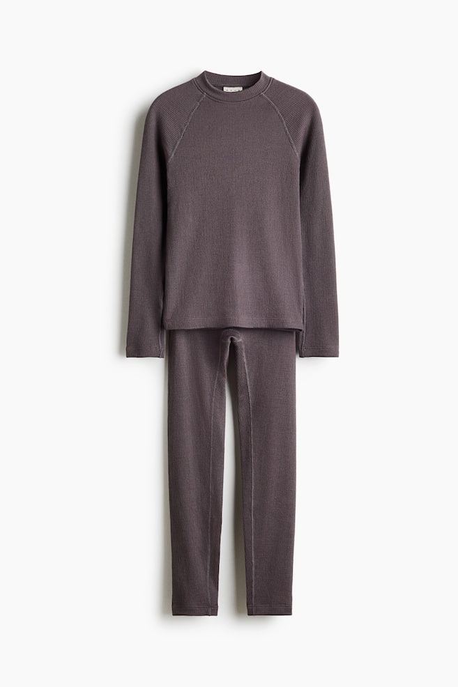 A two-piece ribbed knit lounge set in a dark purple-grey color is hanging facing front, featuring a long-sleeve top with a crew neck and raglan sleeves, paired with matching slim-fit leggings. - 1