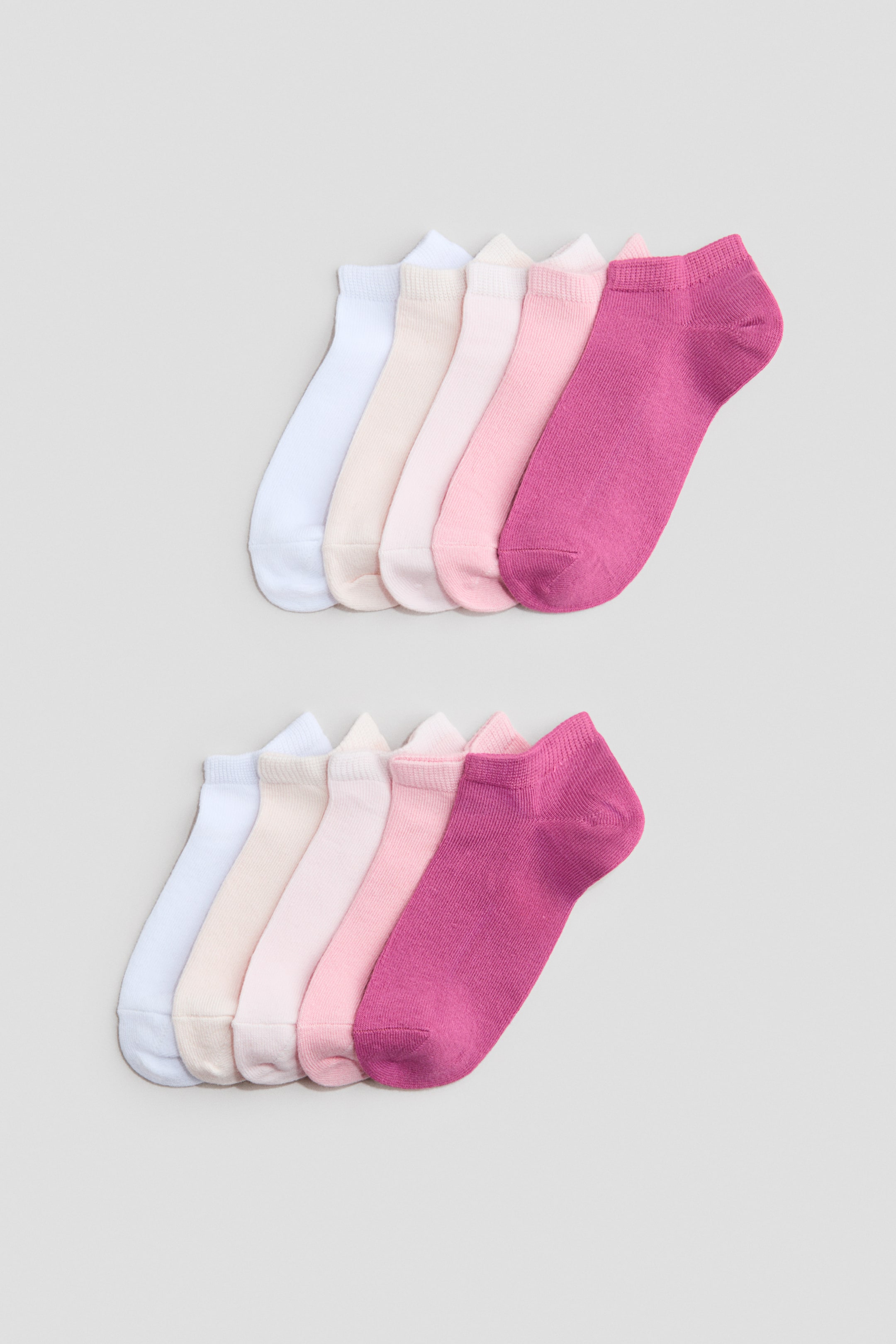 View larger image: Trainer socks are available in two sets, with each set showcasing five socks in a colour gradient from white to cream, light pink, medium pink, and dark pink. Each sock boasts a soft, fine-knit texture with visible elastication around its top.