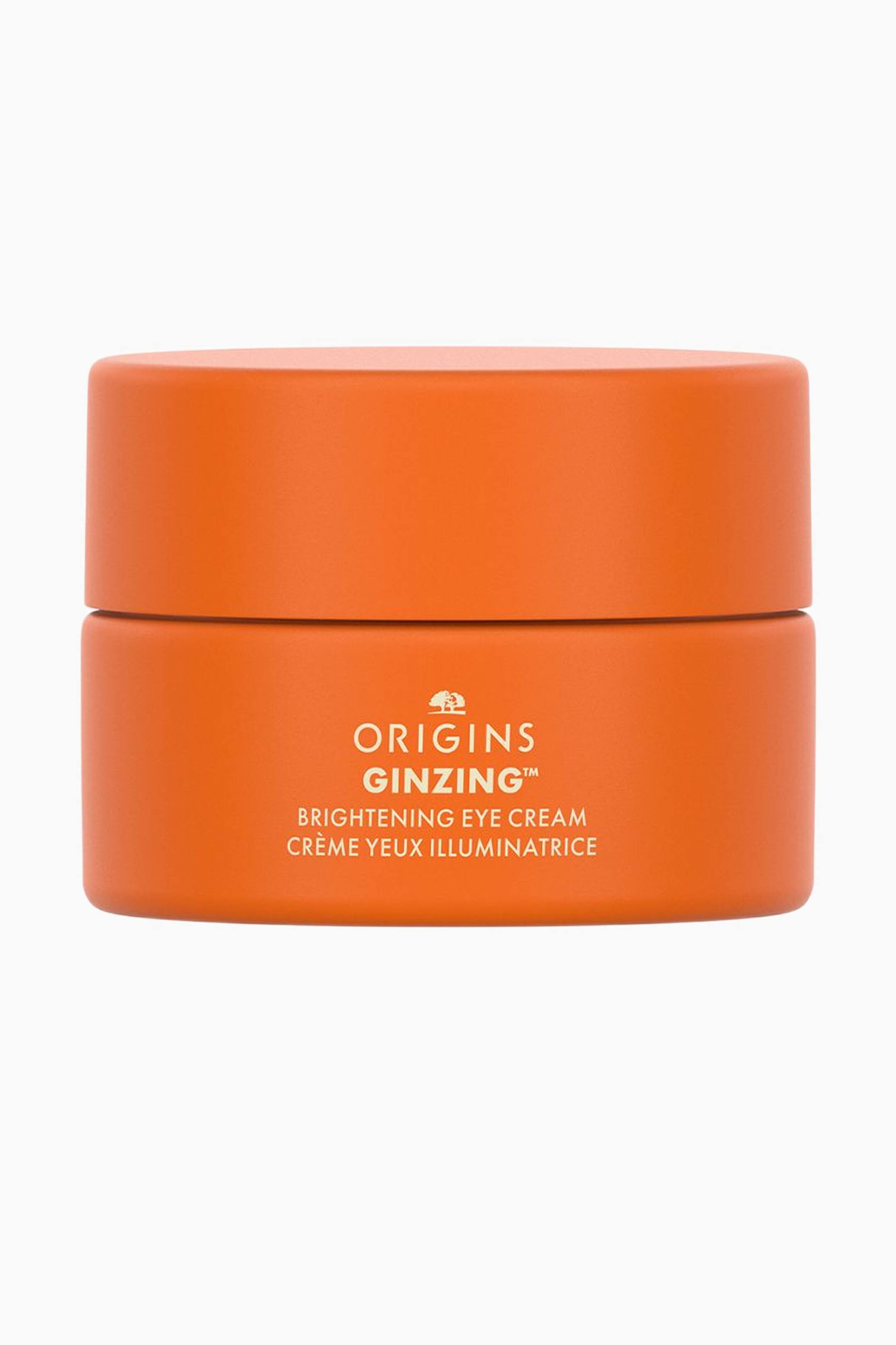 Näytä suurempi kuva: Pieni, sylinterimäinen mattapintainen oranssi Origins GinZing Brightening Eye Cream -purkki seisoo pystyssä ja osoittaa eteenpäin, ja sen yhteensopiva oranssi kansi on suljettu. Purkin etupuolella on kermanväristä tekstiä, jossa lukee "ORIGINS GINZING? BRIGHTENING EYE CREAM" ja sen alla "CR�ME YEUX ILLUMINATRICE" brändin puulogon alla.