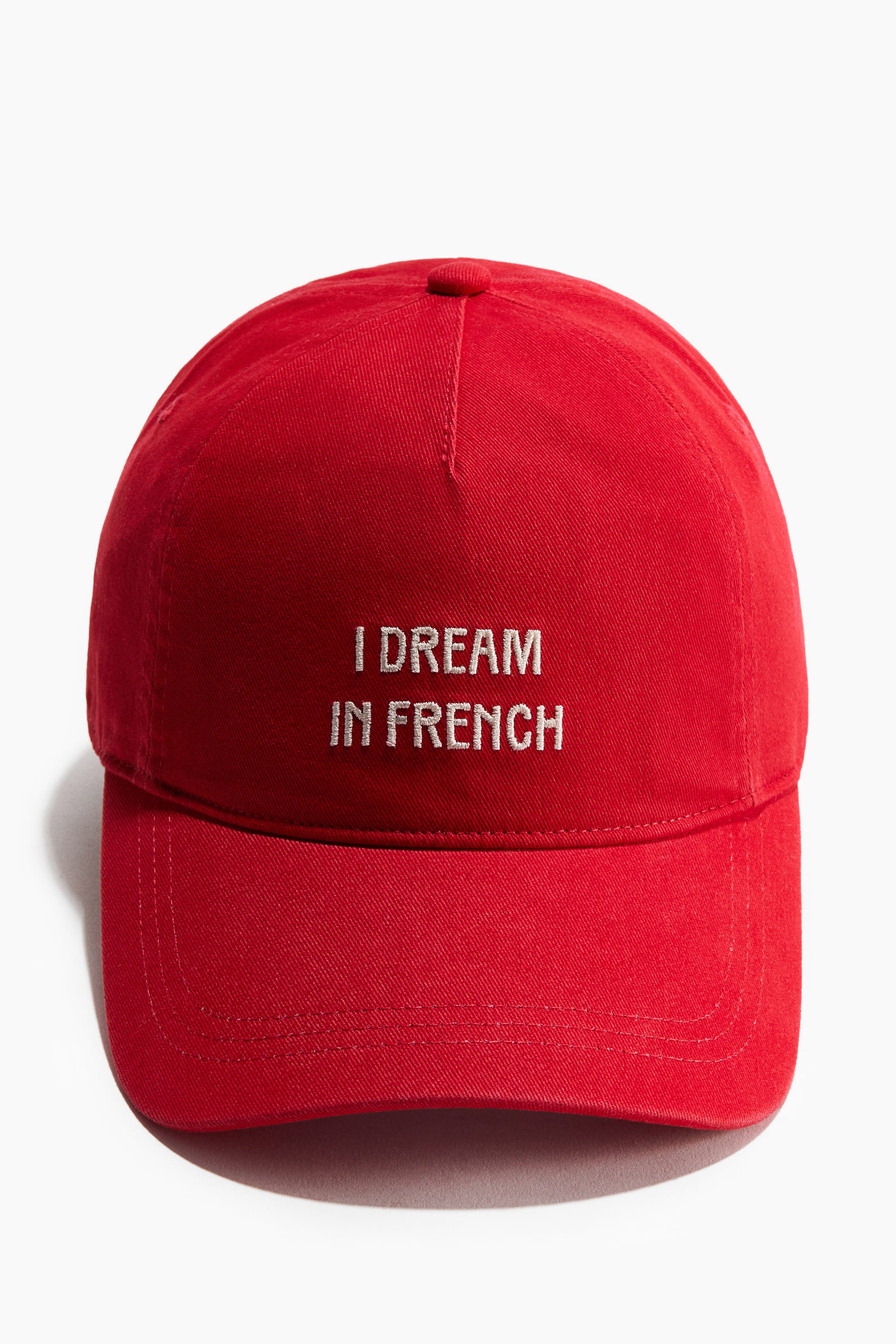 Ver imagen más grande: Una gorra roja de sarga de algodón está orientada hacia adelante, con texto bordado en blanco "I DREAM IN FRENCH" en su panel frontal. Presenta un diseño clásico de gorra de béisbol con una visera estructurada.