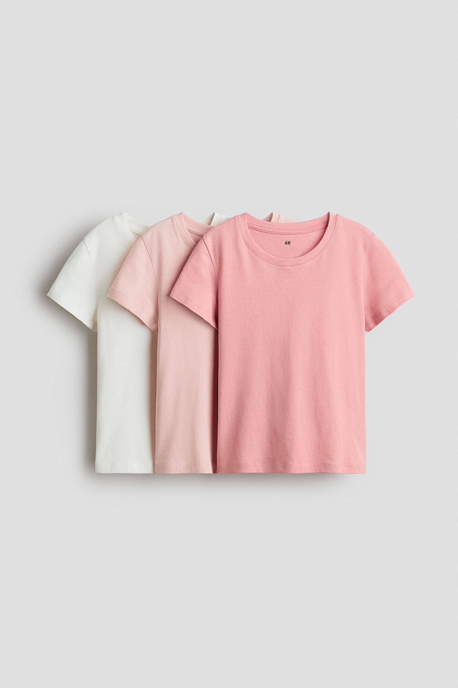A set of three short-sleeved t-shirts is presenting its front view, featuring white, light pink, and pink colors. Each t-shirt is designed with a round, ribbed neck and a straight hem.