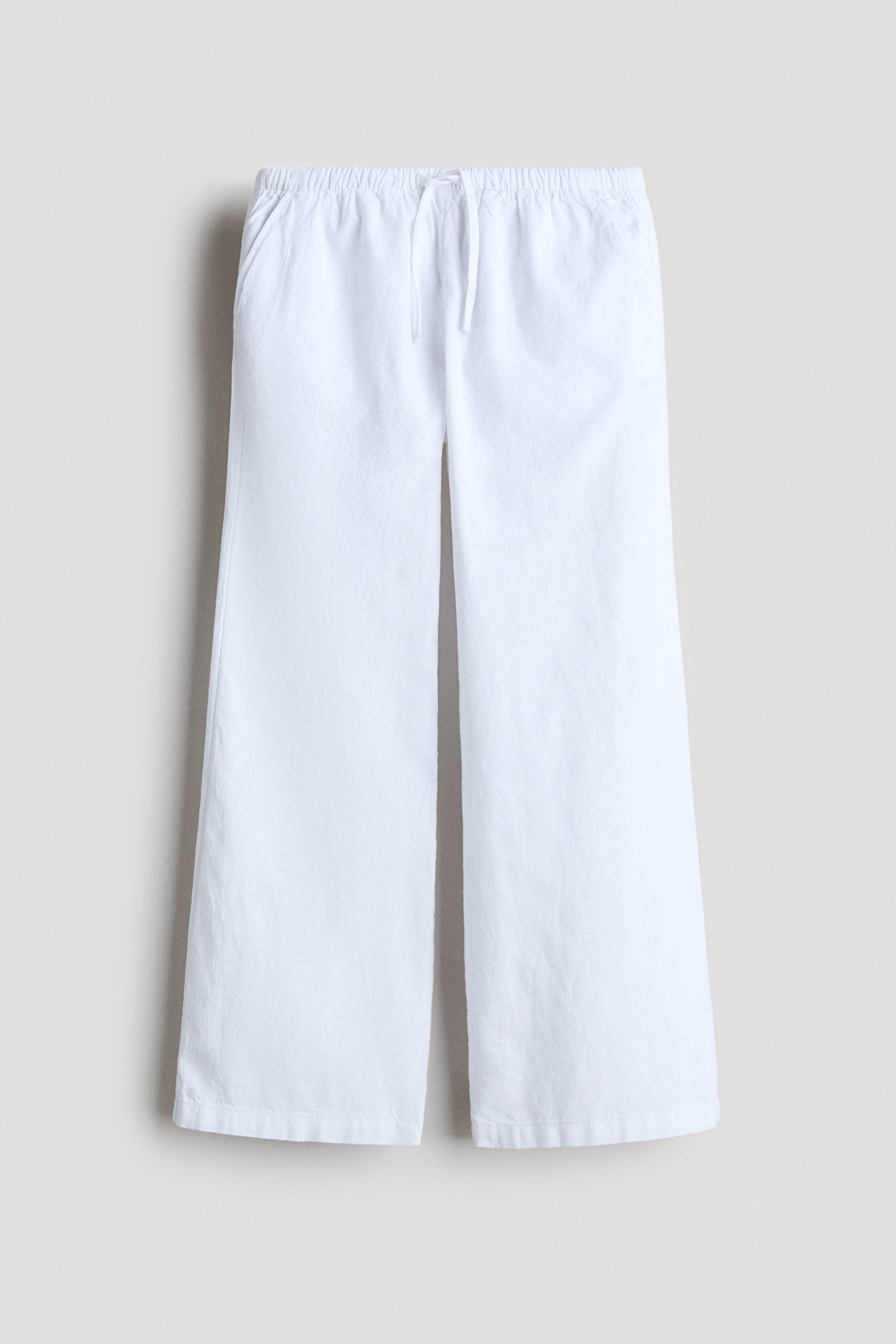 View larger image: White trousers are displayed at the front, showcasing a soft cotton and linen blend weave. They come with an elasticated, drawstring waist, diagonal side pockets, and straight legs.