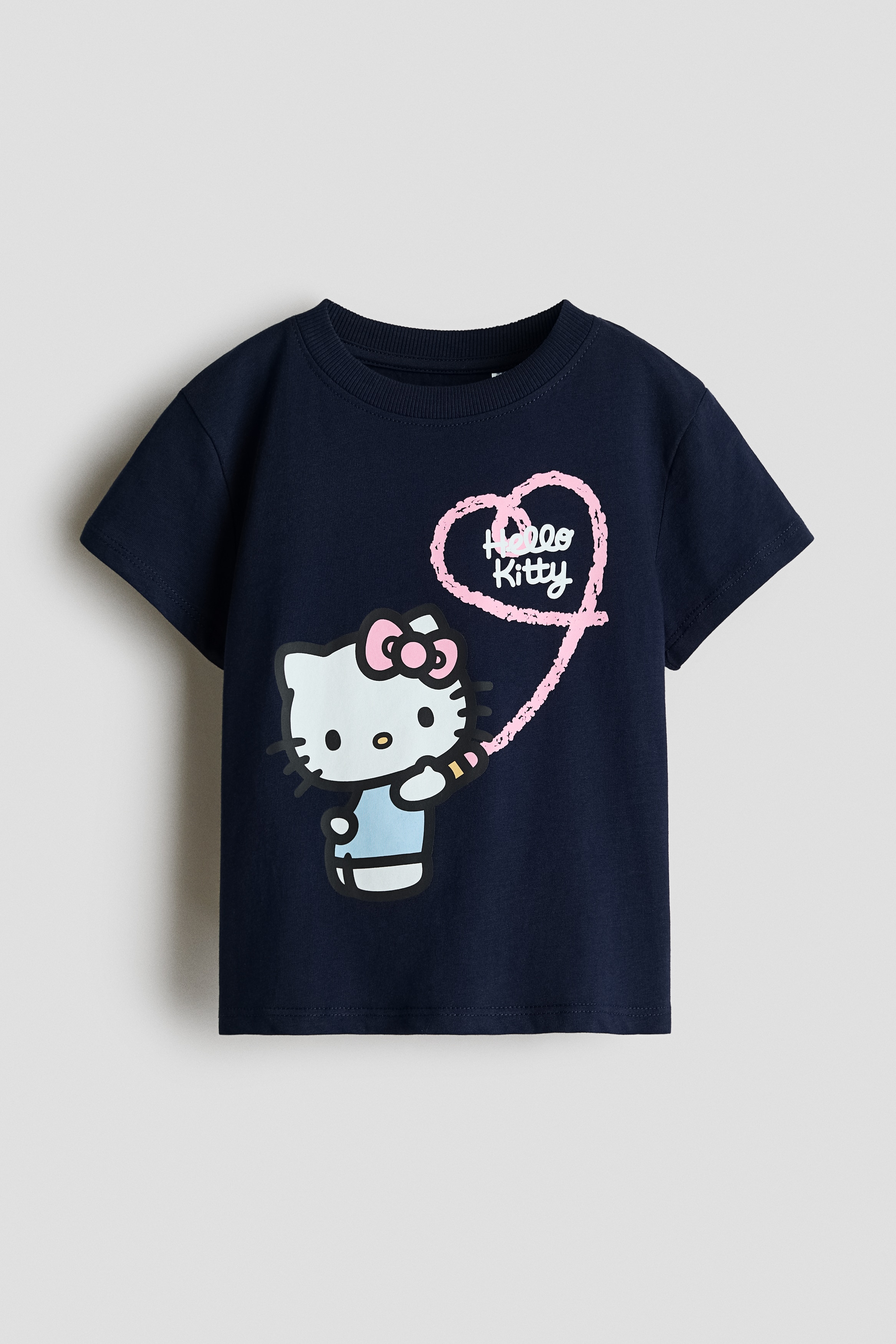 A dark blue cotton jersey T-shirt featuring a Hello Kitty graphic print on the front is worn by the model. The T-shirt has a round, rib-trimmed neckline and short sleeves, and is styled with blue denim jeans.