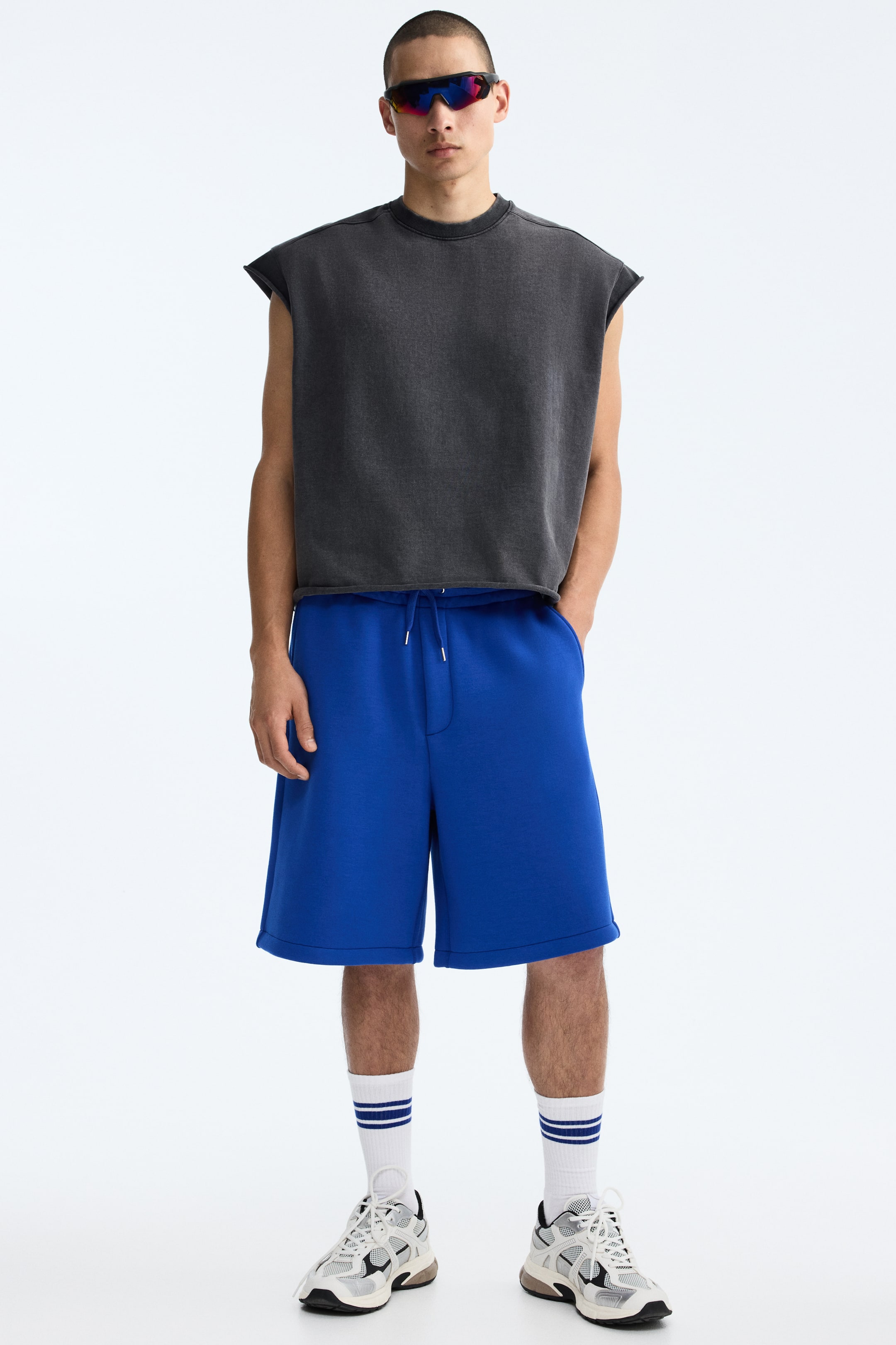 View larger image: Blue sweatshorts offer a relaxed fit with an elastic waistband and a visible drawstring, featuring side pockets and extending to just above the knees.