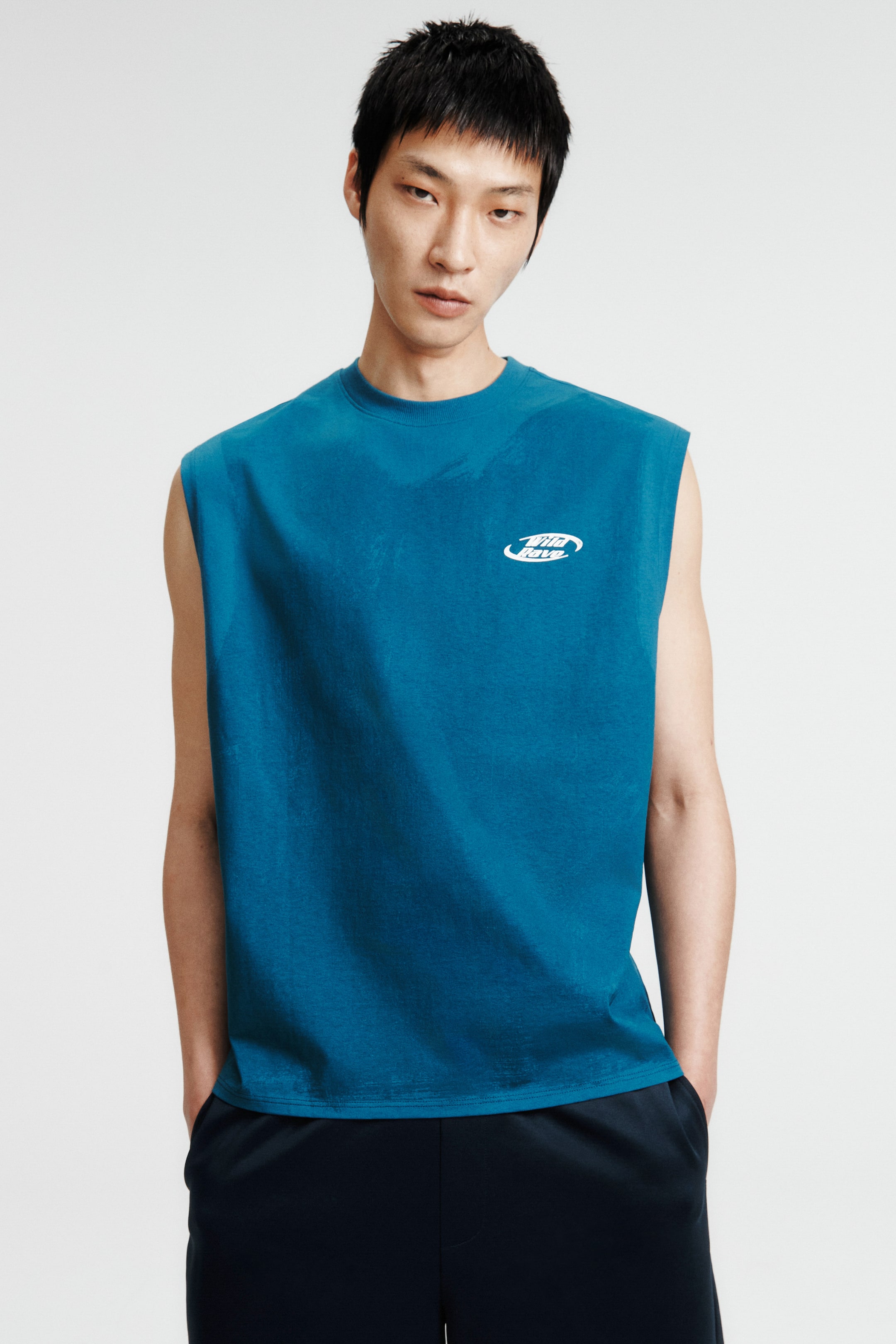 View larger image: The model is wearing a teal vest top, showcasing a round neckline with rib trim, deep armholes, and a white print motif on the front chest. This loose-fitting top features a straight-cut hem.