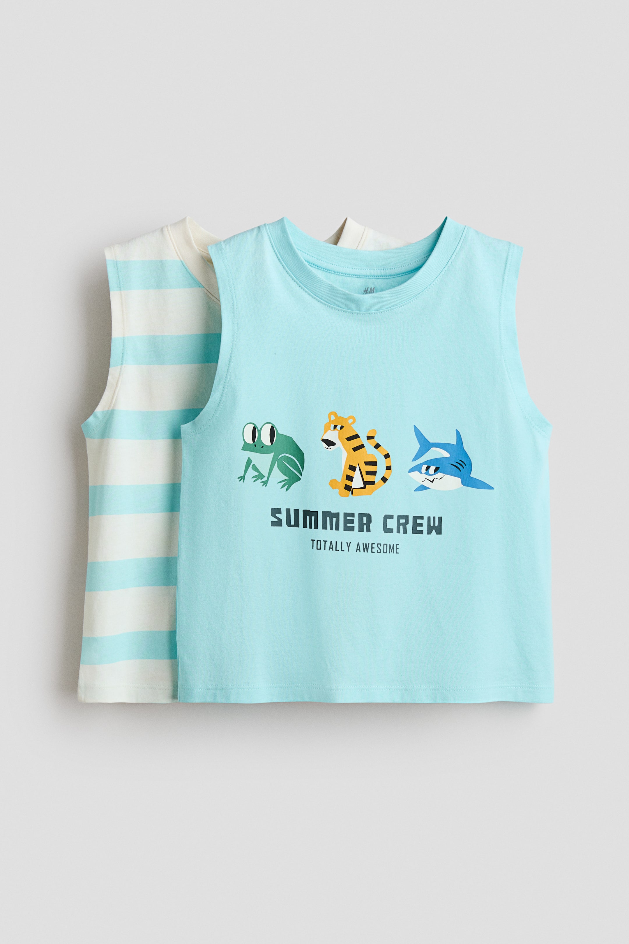View larger image: Two sleeveless tops are showcased with their front sides visible. The top in the front is light blue and features a graphic print of a green frog, an orange tiger, and a blue shark, with the words "SUMMER CREW TOTALLY AWESOME" printed below. The second top, partially visible behind, has a cream base adorned with light blue horizontal stripes.