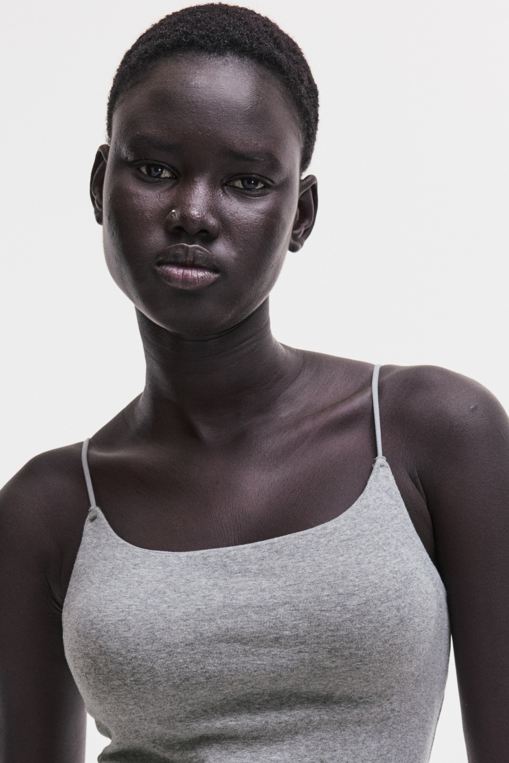 View larger image: A light gray camisole featuring a scoop neckline, thin spaghetti straps, and a ribbed knit texture, cut to fit closely to the torso.