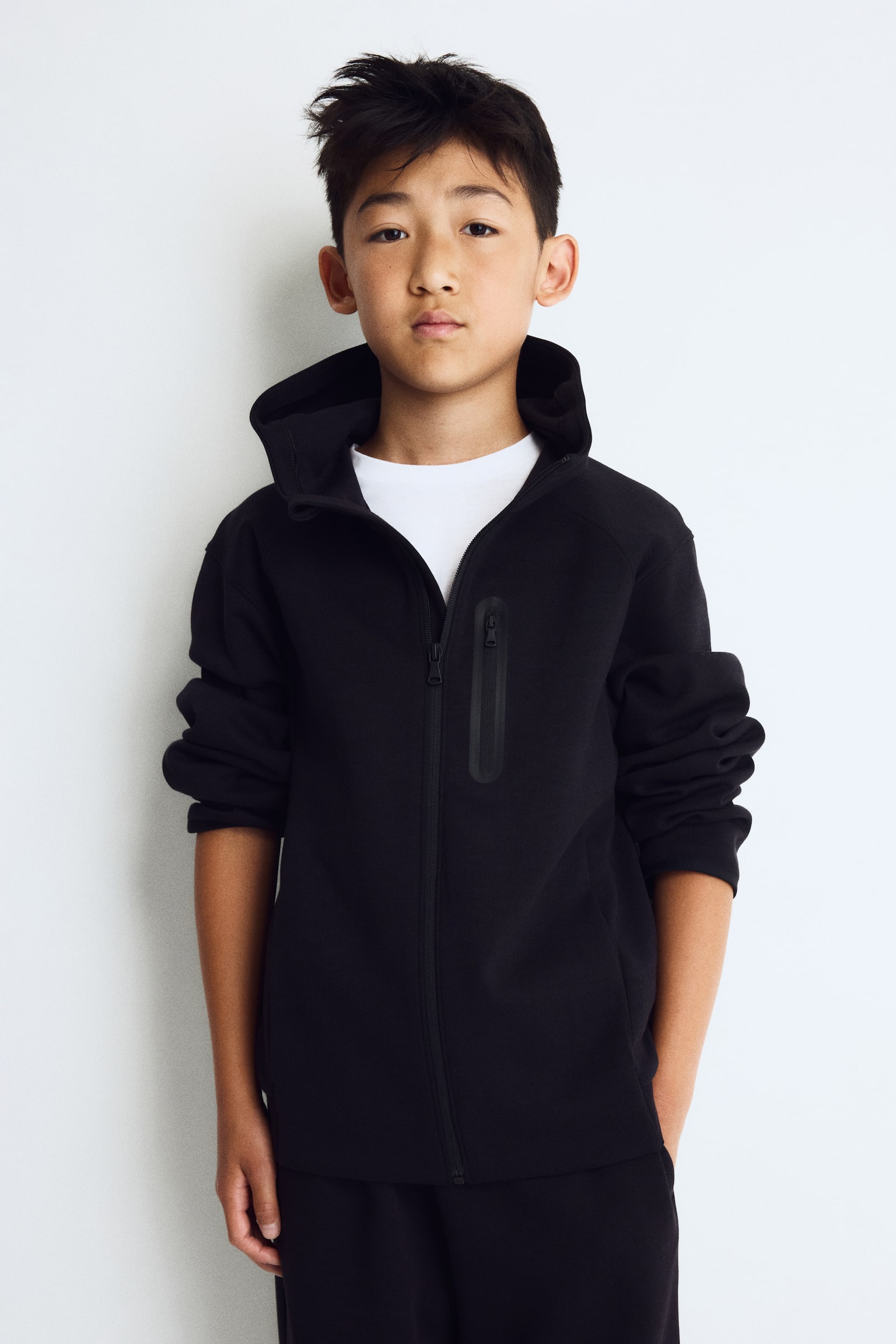 A black hoodie is facing forward, featuring a full-zip fastening, a hood, and a vertical zippered chest pocket on the wearer's left side. It showcases long raglan sleeves with banded cuffs and a banded hem, along with subtle "DRYMOVE" text vertically on the lower right sleeve. - 1