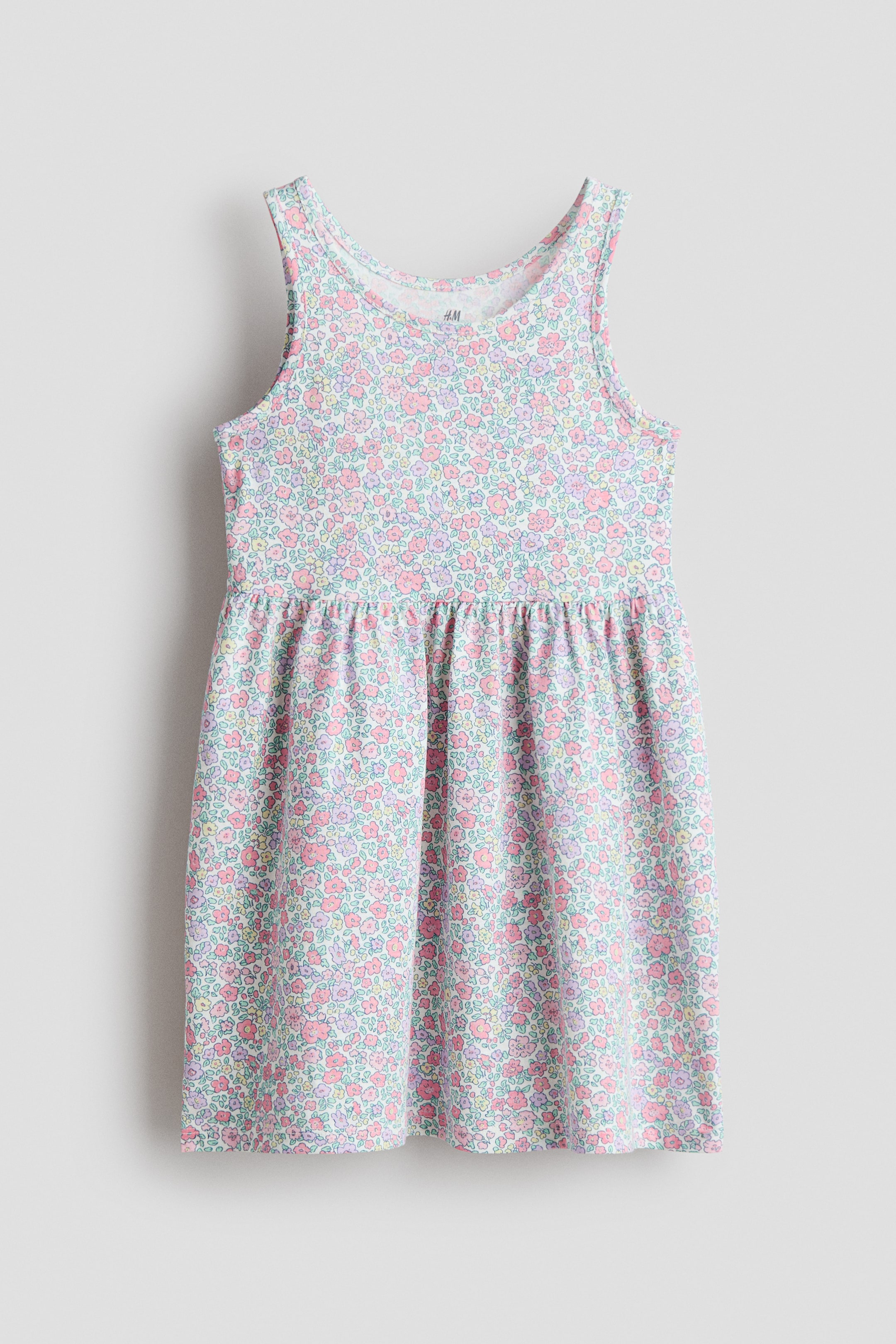 Größeres Bild ansehen: Ein ärmelloses Kleid zeigt seine Vorderansicht und besteht aus weichem, gemustertem Baumwolljersey mit kleinem Blumenmuster in Pastellfarben; es ist mit rundem Ausschnitt, einer in der Taille gerafften Naht und einem sanft ausgestellten Rock gearbeitet.