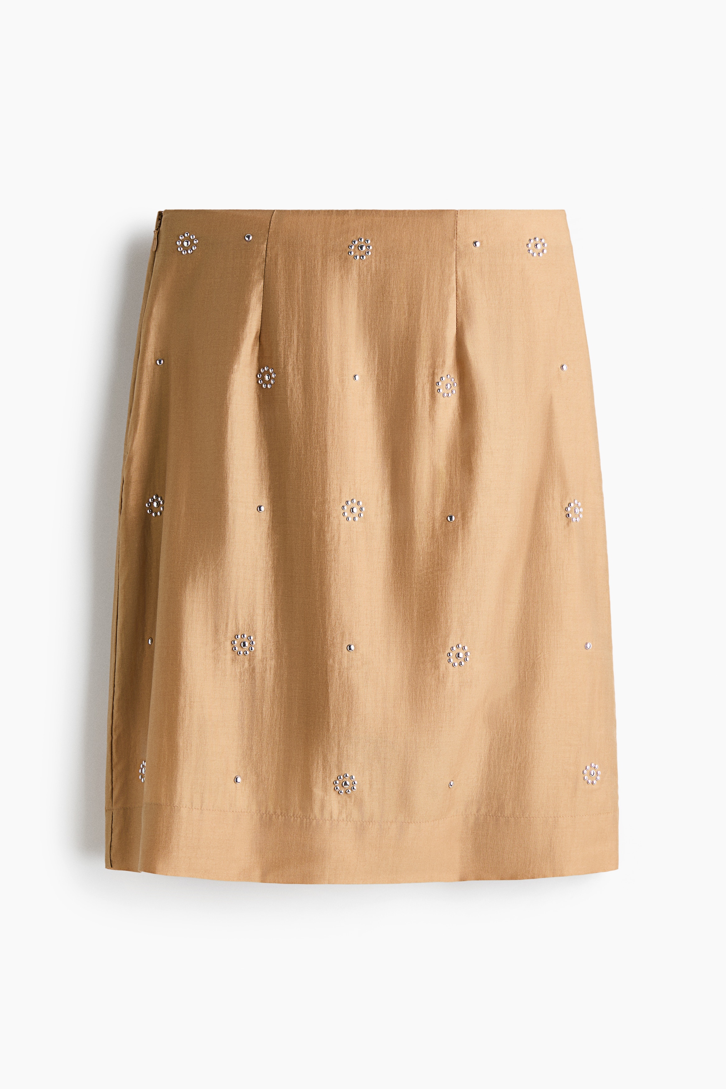 A brown zippered jacket with white floral embroidery on the chest, a high collar, and an elasticized hem and cuffs is worn by the model. The jacket is styled with a beige embellished midi skirt, a brown belt with a large buckle, and matching brown boots.