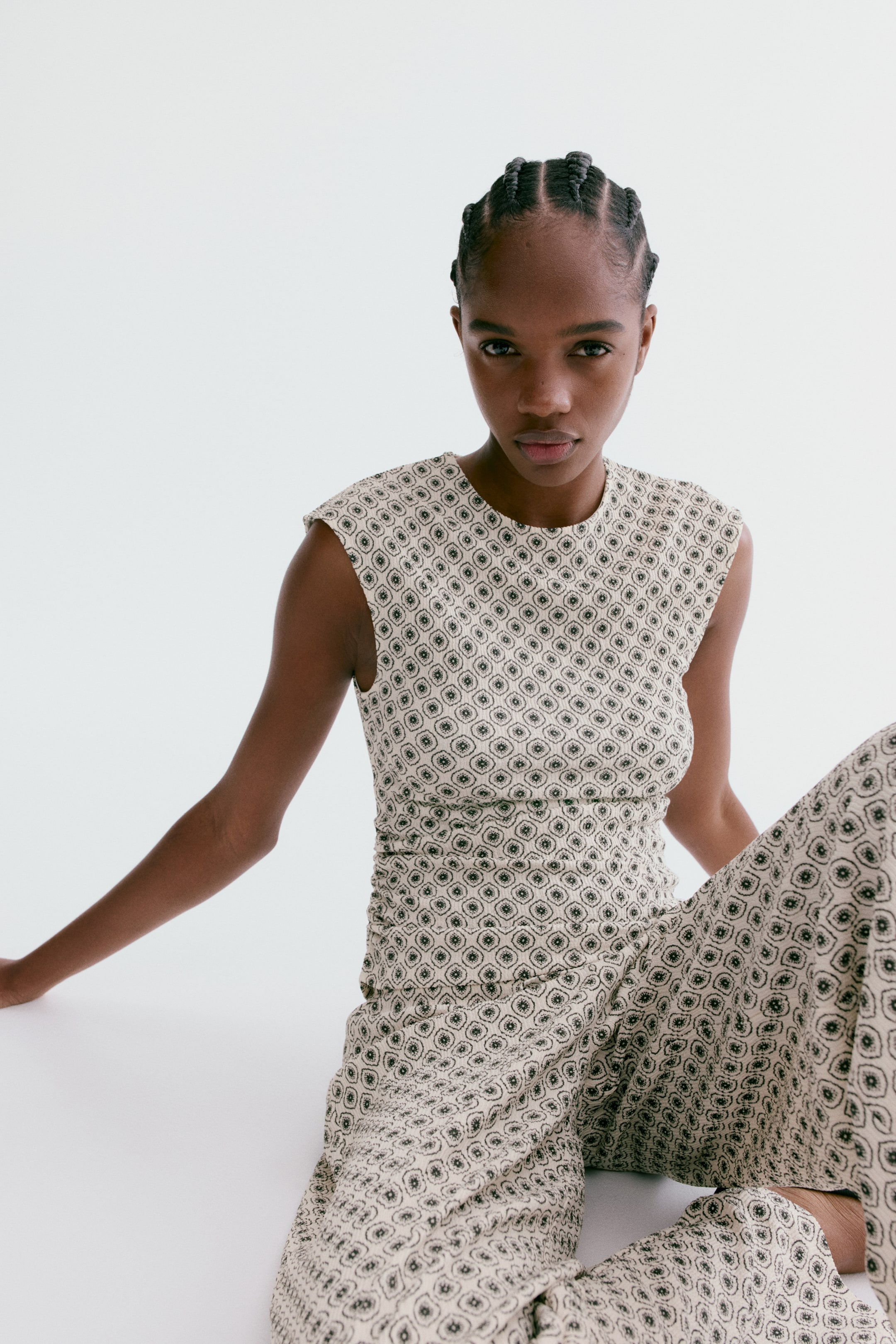 View larger image: A sleeveless top featuring a light-coloured fabric with a repeating dark geometric mosaic pattern, a round neckline, and structured shoulders, also showing ruching along its side. Matching wide-leg trousers showcase the same geometric mosaic pattern and a relaxed fit.