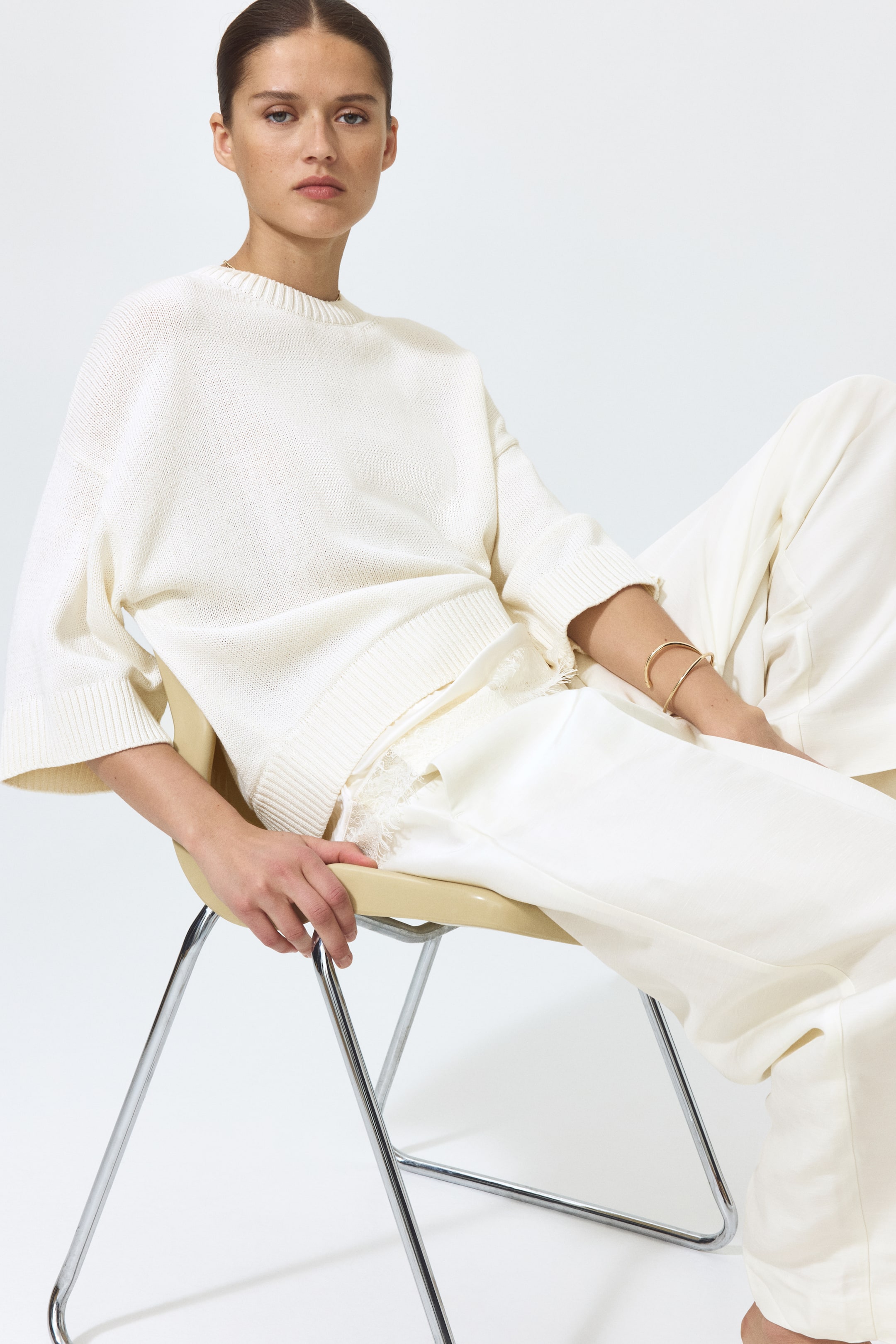 View larger image: A cream-coloured crew neck jumper features a relaxed fit with three-quarter length sleeves and ribbed cuffs, its ribbed hem revealing a cream garment with lace trim underneath.