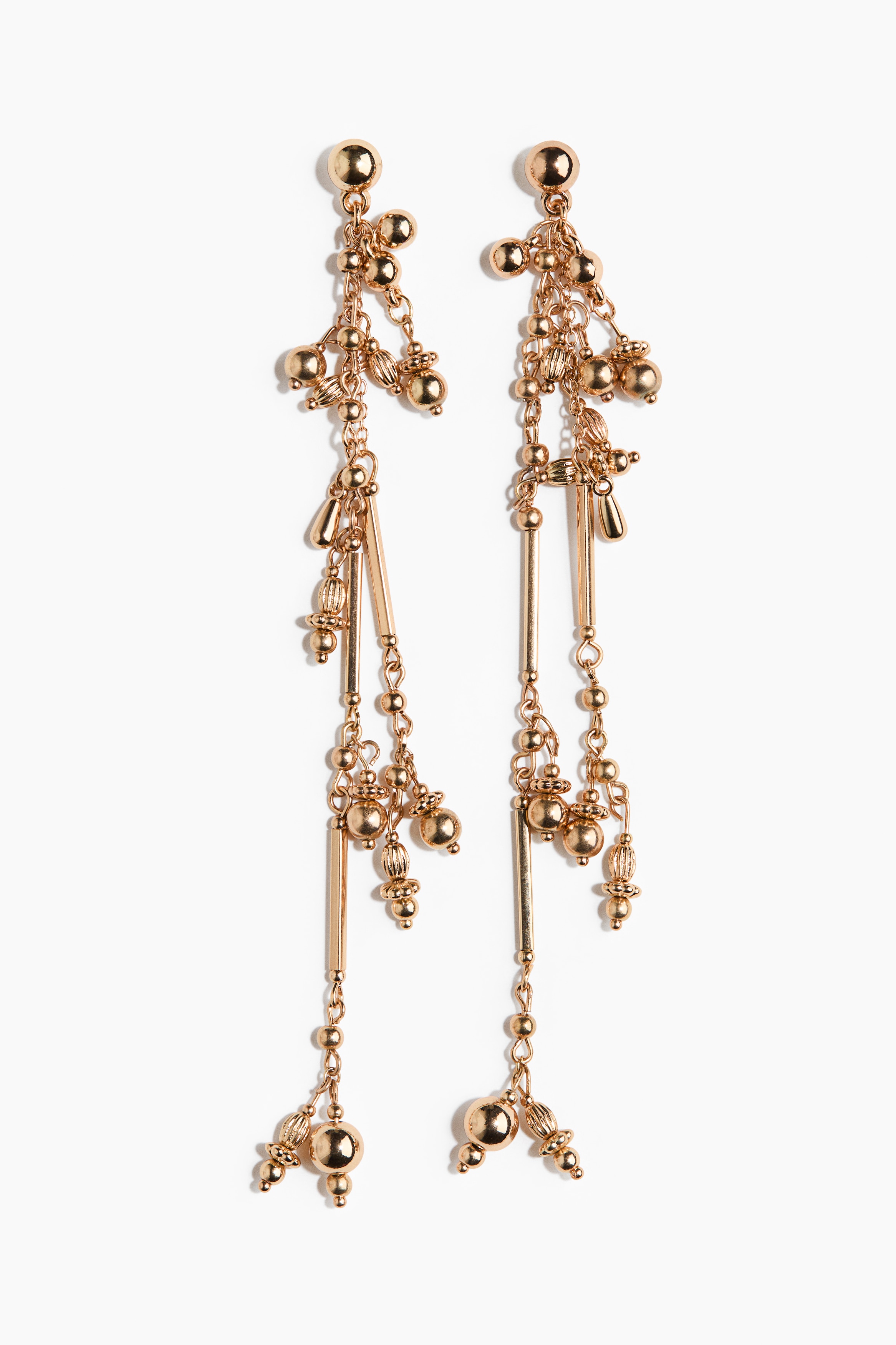 Long dangle earrings featuring gold-colored beads in various textured and smooth designs are being worn by the model. The multi-strand earrings hang down from delicate chains, incorporating small bars and spherical elements that drape alongside the neck.