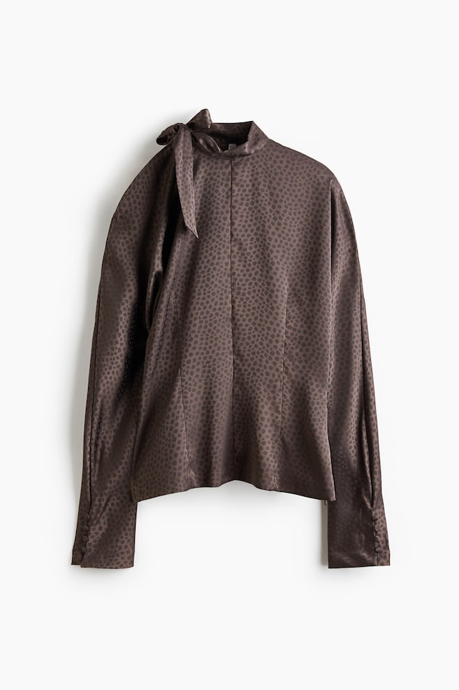 Une blouse marron foncé arbore un motif jacquard subtilement tacheté sur toute sa surface. Elle est conçue avec un col montant noué en un nœud et des manches longues avec des poignets boutonnés. - 1