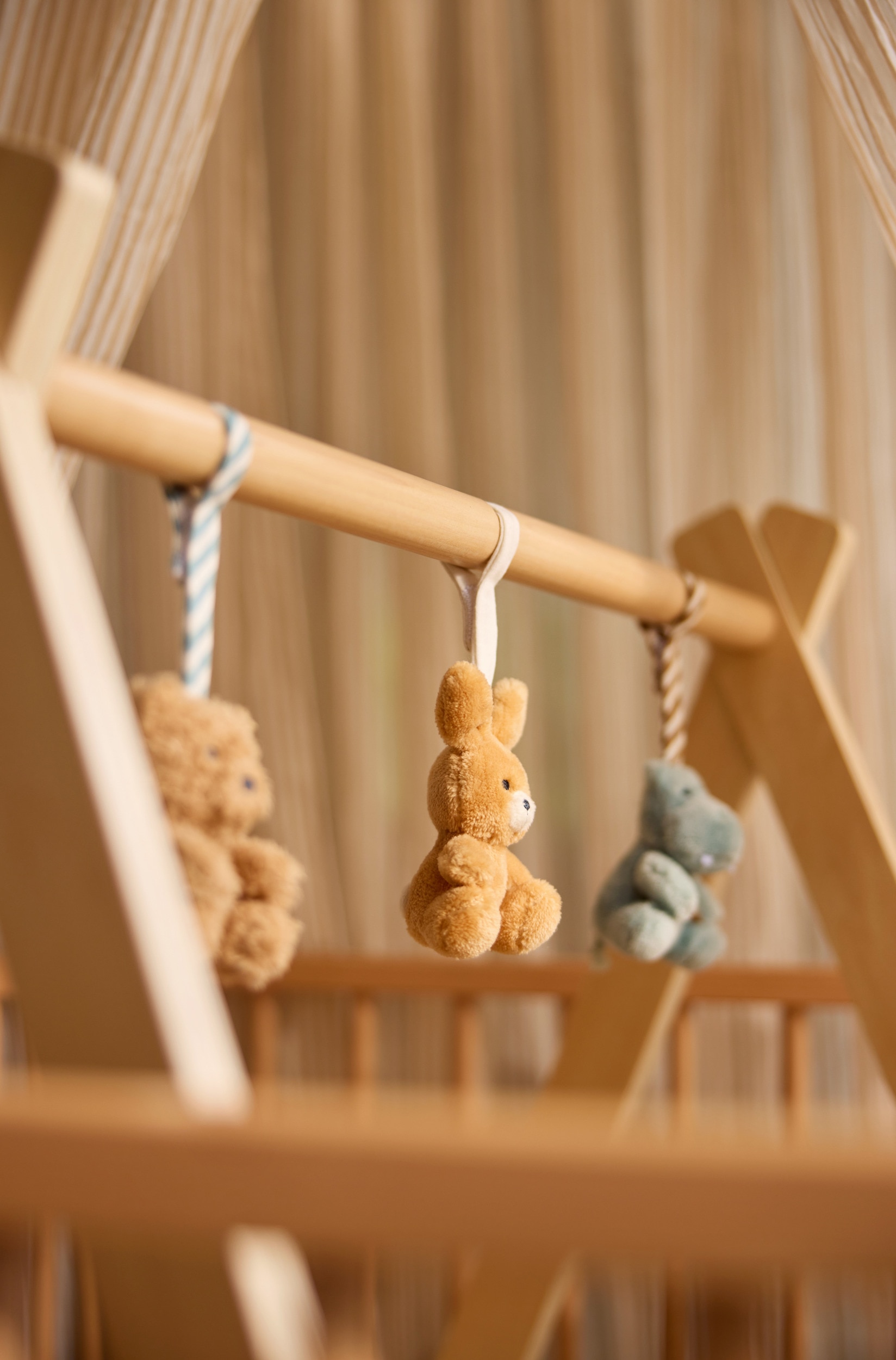 Un cadre de gym dâÃ©veil pour bÃ©bÃ© en bois est dressÃ© verticalement, avec une structure en bois naturel de teinte claire et des pieds en A soutenant une barre ronde horizontale. La barre supÃ©rieure prÃ©sente trois petites encoches sculptÃ©es sur sa face supÃ©rieure.