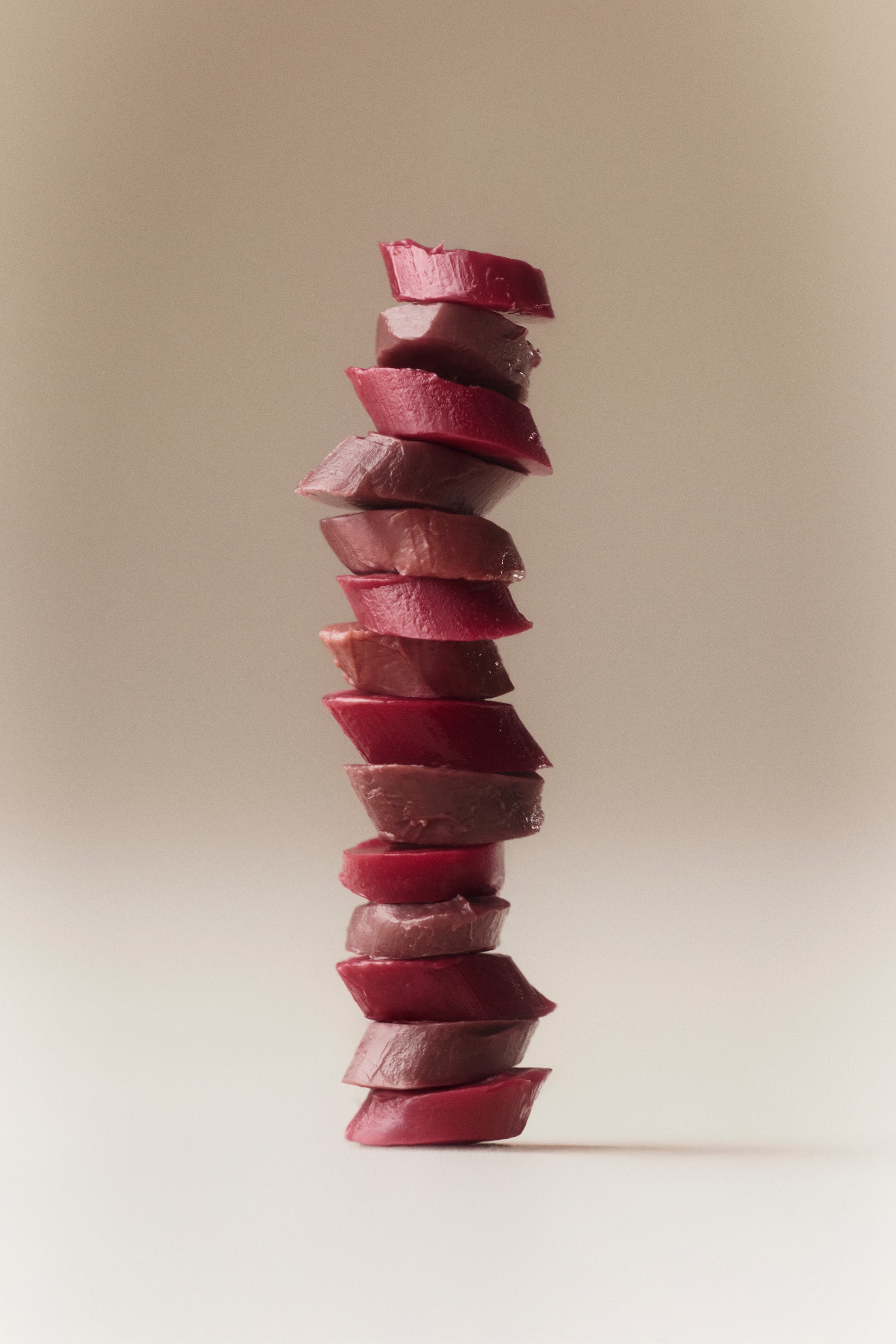 View larger image: A tall, vertical stack of uniquely shaped lip gloss balm pieces is displayed, showcasing alternating reddish-brown and muted brown shades. Each piece is slightly tilted, adding to the leaning arrangement.