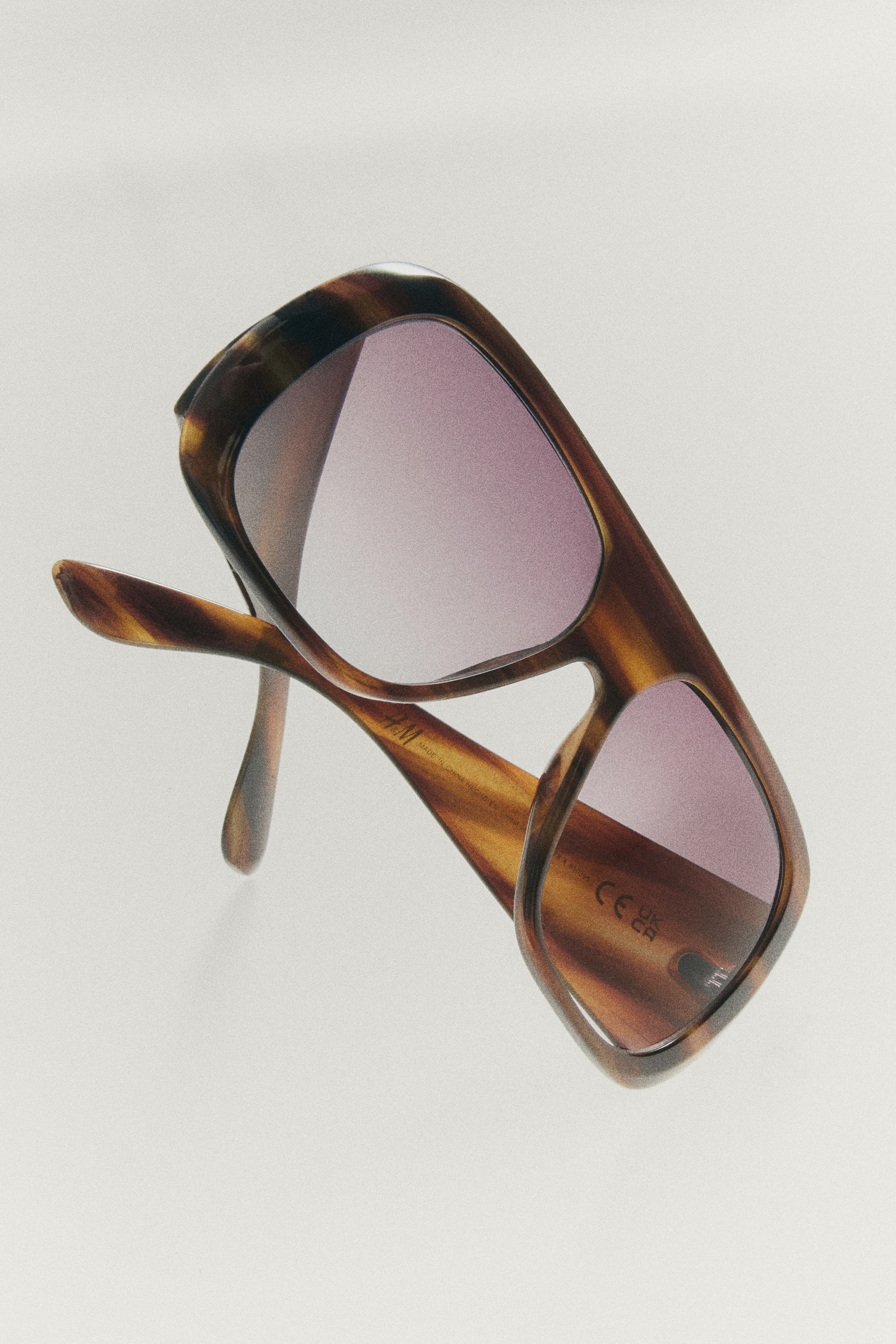 View larger image: Shield sunglasses featuring thick, tortoiseshell-patterned plastic frames and light purple-tinted lenses are shown from an angled front view. The oversized design displays wide temple arms and a flat-top bridge.