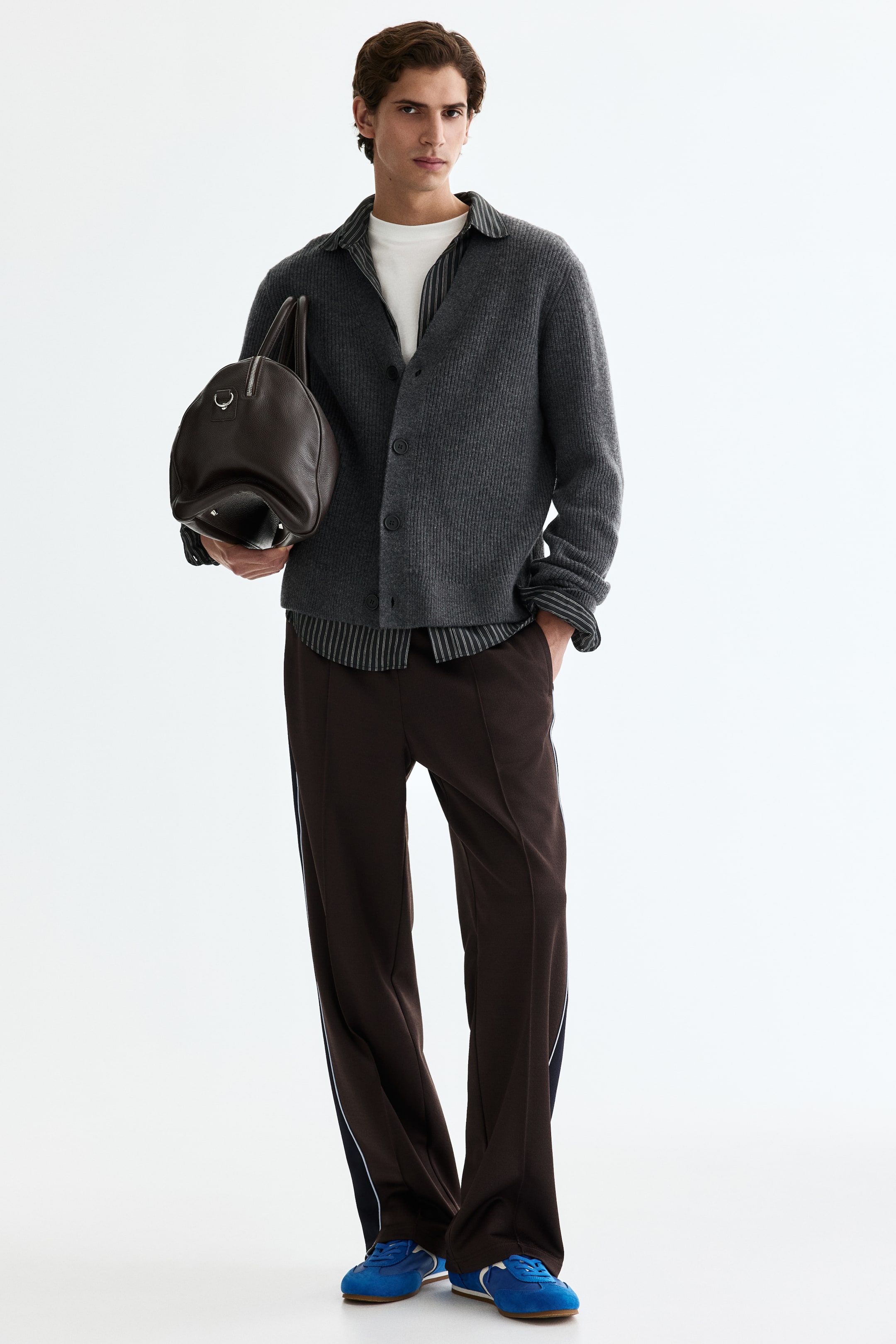 View larger image: A grey ribbed knit cardigan is worn open over a striped shirt and white t-shirt, featuring a pointed collar and dark button-front fastening.