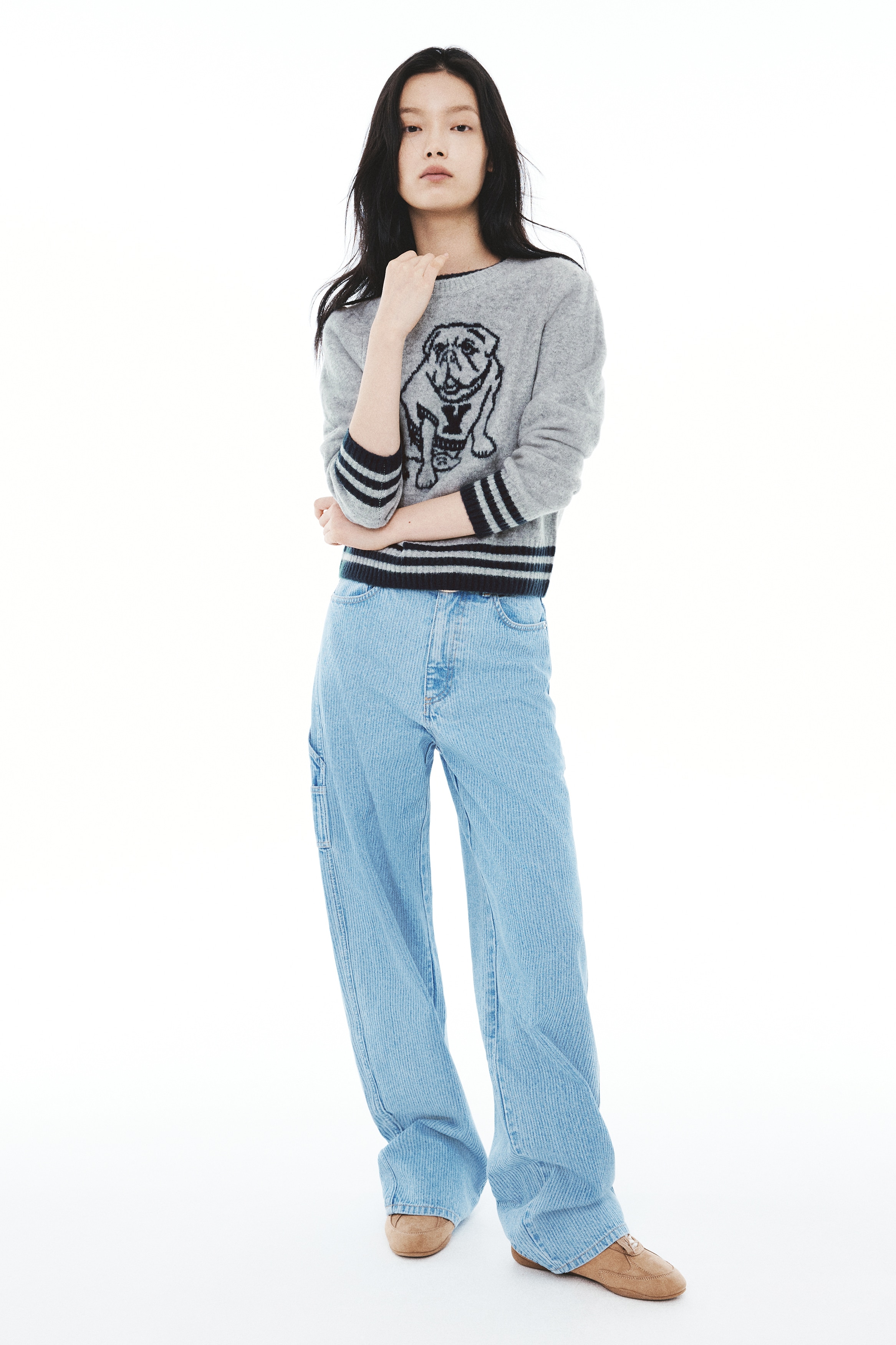 A light grey knitted jumper is shown from the front, featuring a round, rib-trimmed neckline and a central navy blue jacquard-knit bulldog graphic. The long-sleeved garment has ribbed cuffs and a matching ribbed hem, both accented with dark blue horizontal stripes.