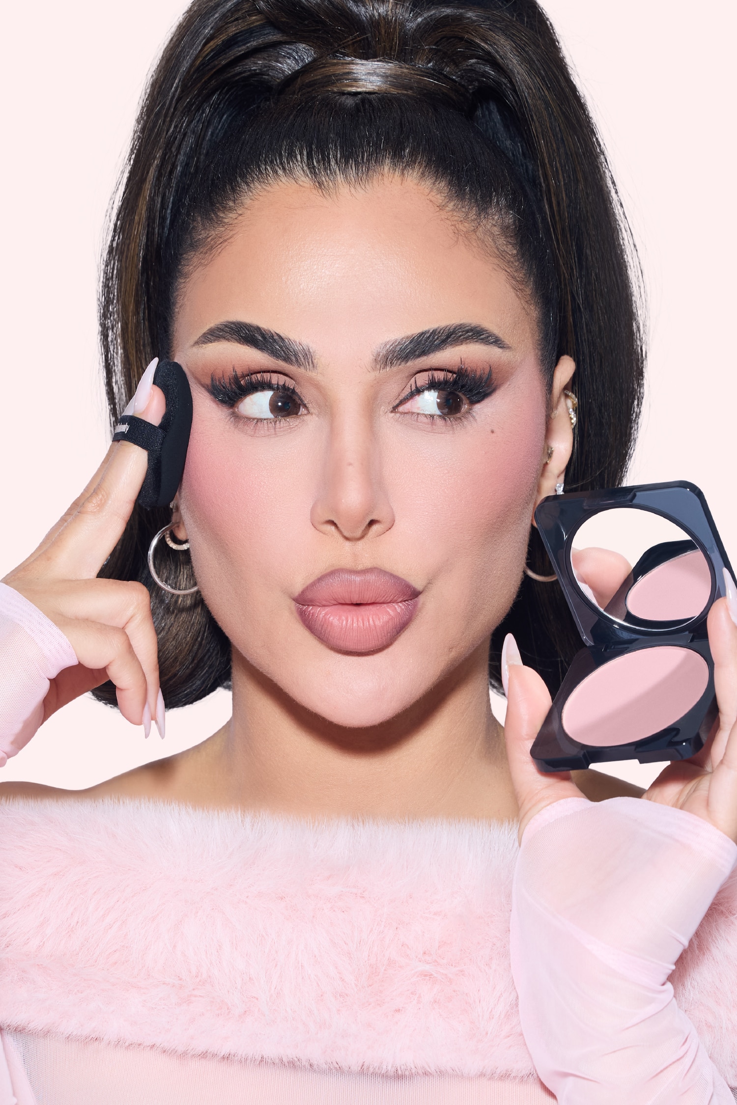 Huda Beauty Easy Bake Pressed Powder-kompakten stÃ¥r Ã¶ppen och visar en rund panna med ljusrosa pressat puder med fin diagonal struktur. Det upphÃ¶jda locket har "hudabeauty"-logotypen, medan ett texturerat prov av det ljusrosa pudret syns bakom kompakten fÃ¶r att visa dess konsistens.