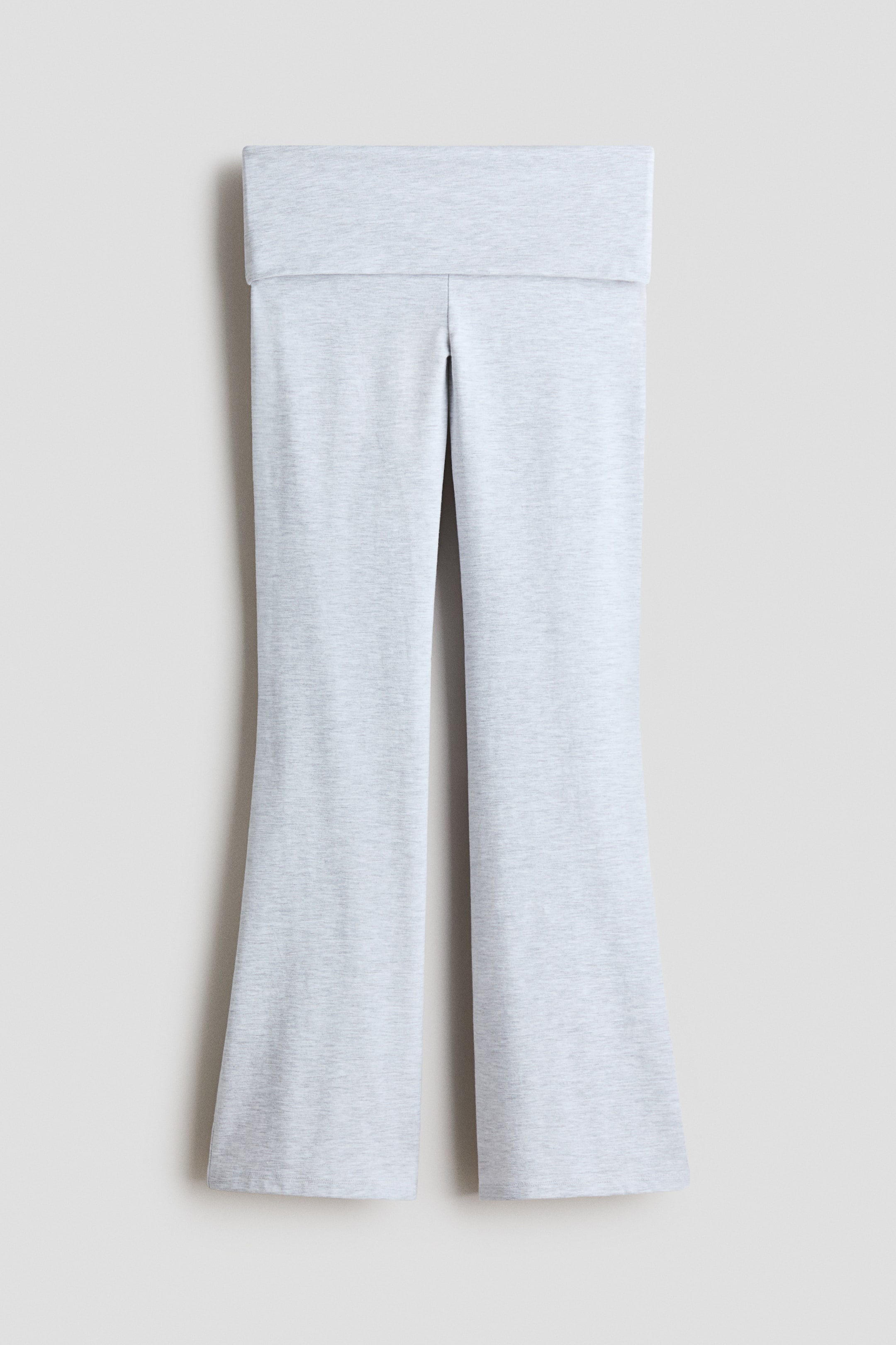 Visualizza immagine più grande: Pantaloni svasati in grigio chiaro melange appesi in una vista frontale, con ampia cintura ripiegata e gambe che si allargano gradualmente verso l’orlo. Il morbido tessuto in maglia jersey mostra una delicata texture melangiata.