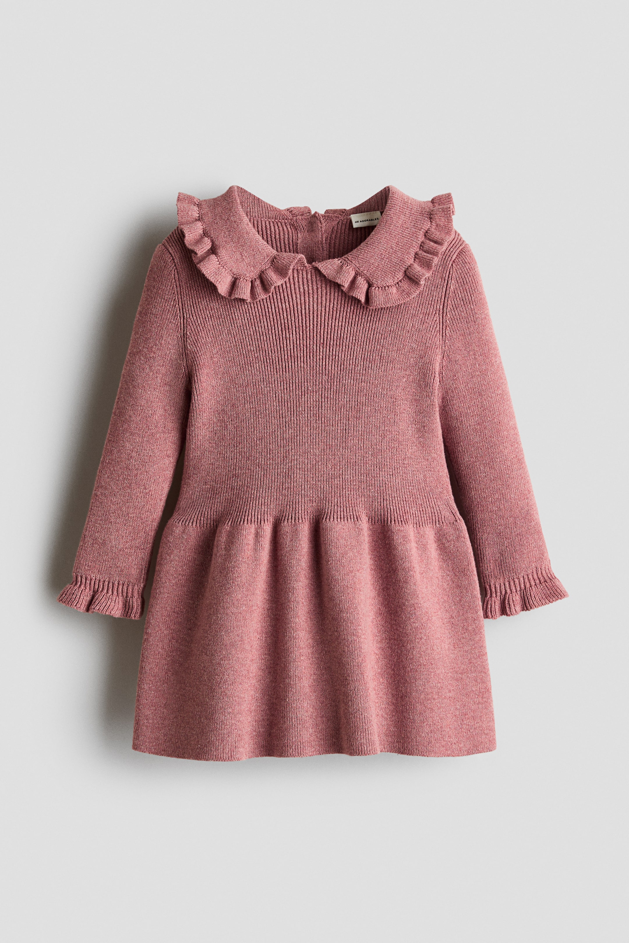 View larger image: A pink knitted dress features a ruffled Peter Pan collar and long sleeves with ruffled cuffs. The bodice showcases a ribbed knit pattern that transitions into a gathered, flared skirt.