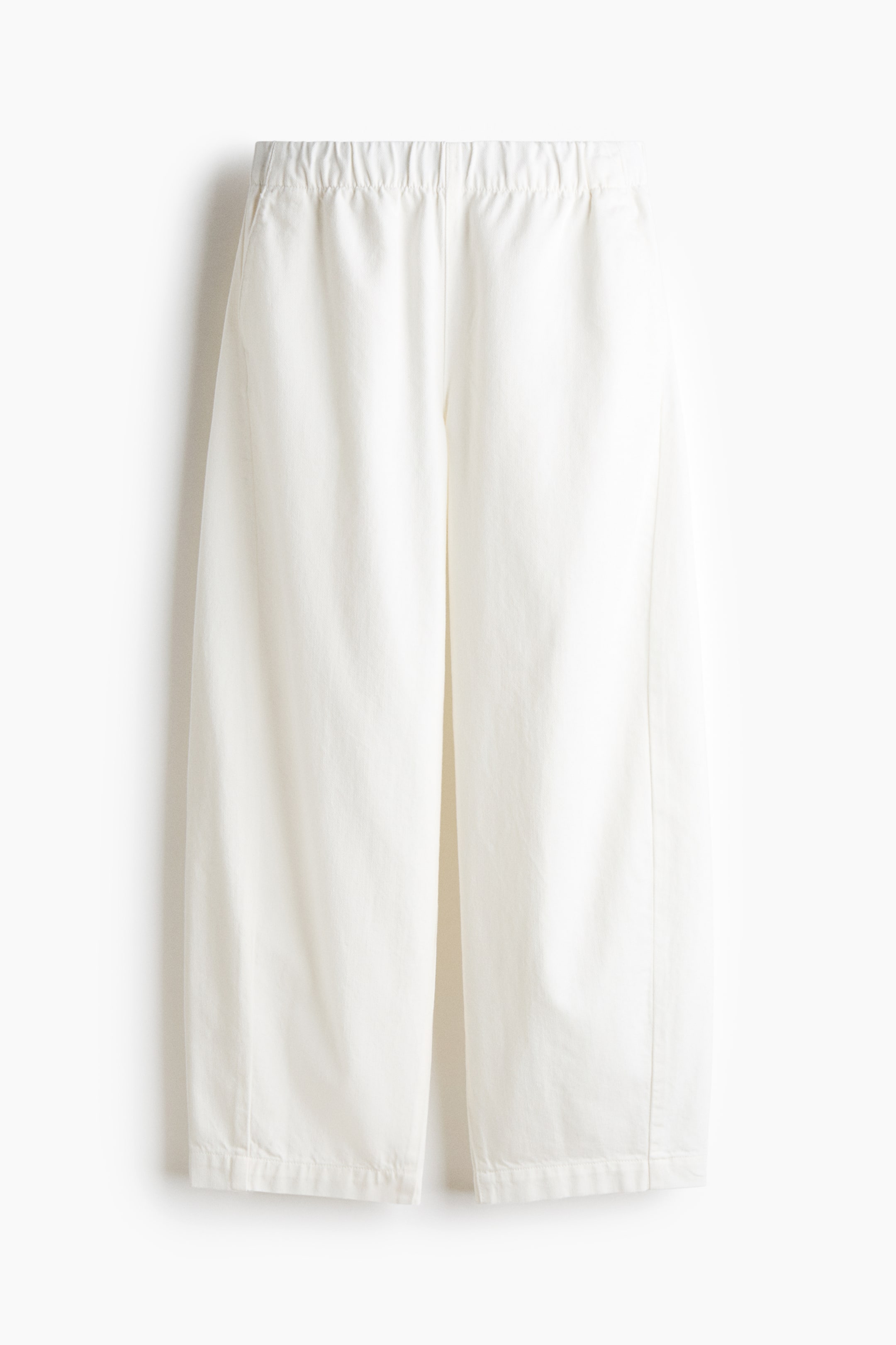 Ver imagen más grande: Pantalones blancos recortados con cintura elástica y piernas anchas. La vista frontal muestra bolsillos laterales visibles y costuras verticales que recorren las piernas.