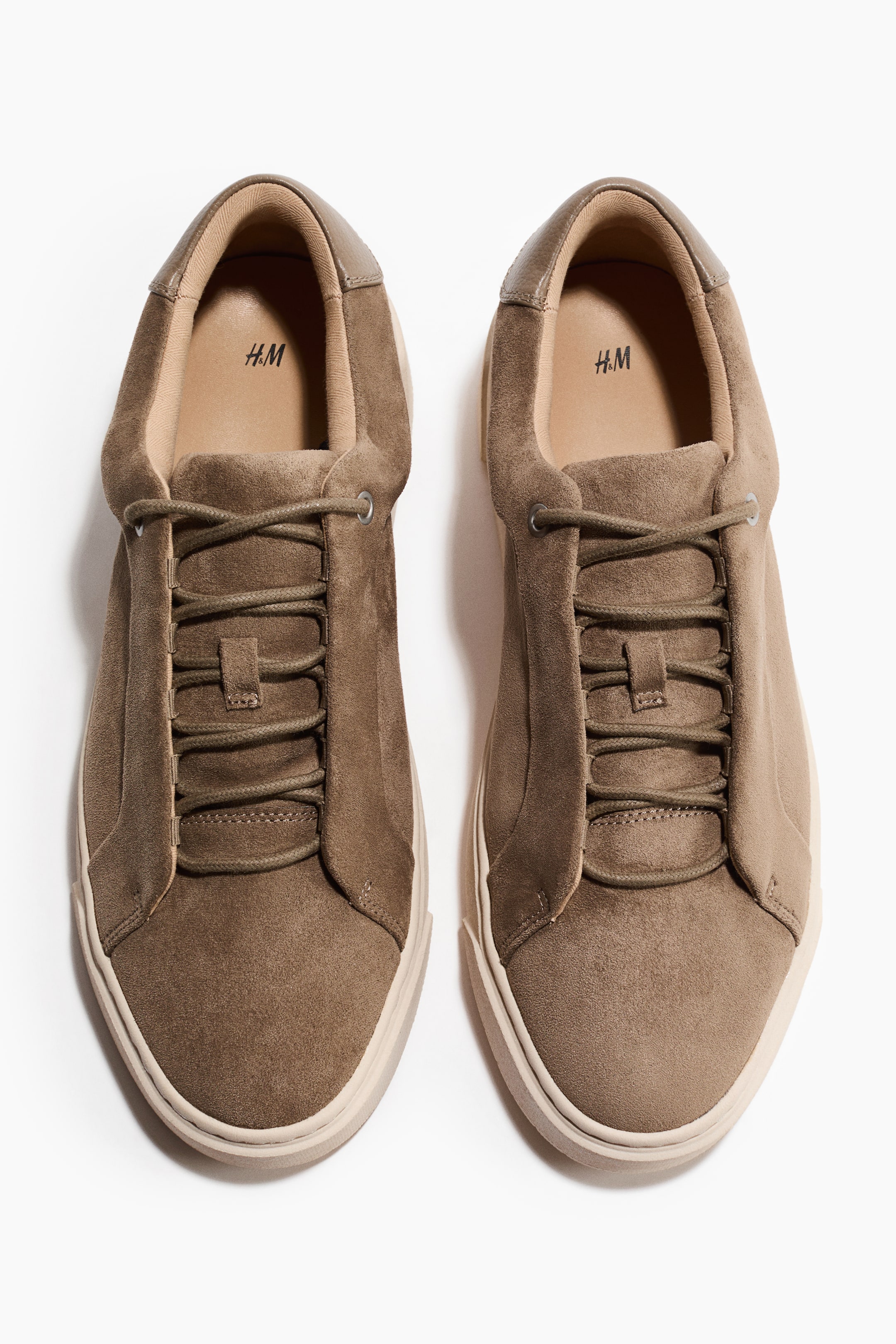 Größeres Bild ansehen: Zwei khakibraune Sneaker aus Wildleder sind FRONT nebeneinander positioniert. Sie verfügen über passende Schnürsenkel, die durch sechs Paar Ösen gefädelt sind, und eine dicke, hellbeige Sohle. Die Innensohle zeigt das Branding „H.M“.