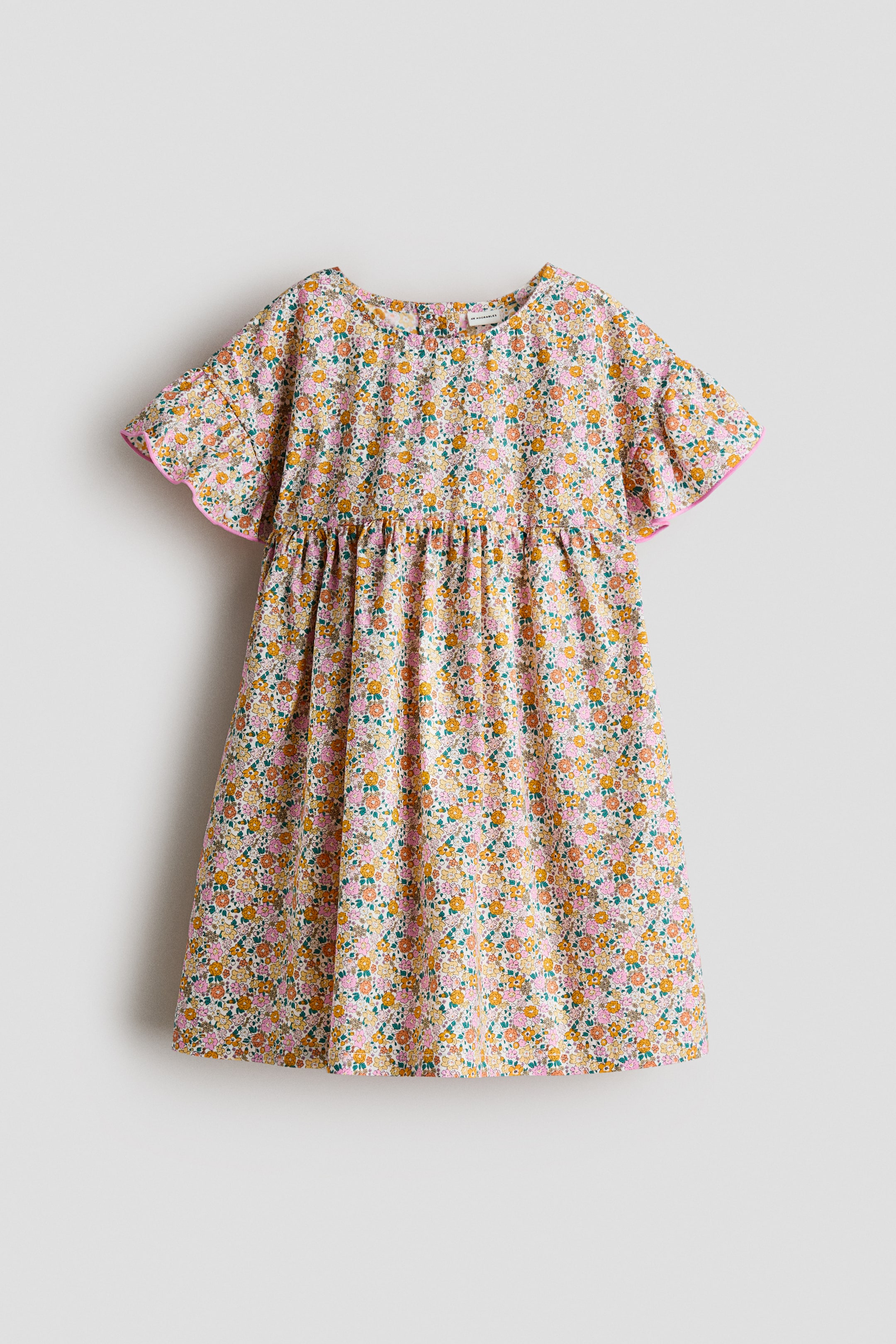 View larger image: The dress is displayed front-facing, highlighting a charming floral print with small pink, yellow, orange, and green flowers. It boasts a round neckline, dropped shoulders, and flutter sleeves finished with pink overlocked edges, with gathers forming at the waist above a flared skirt.