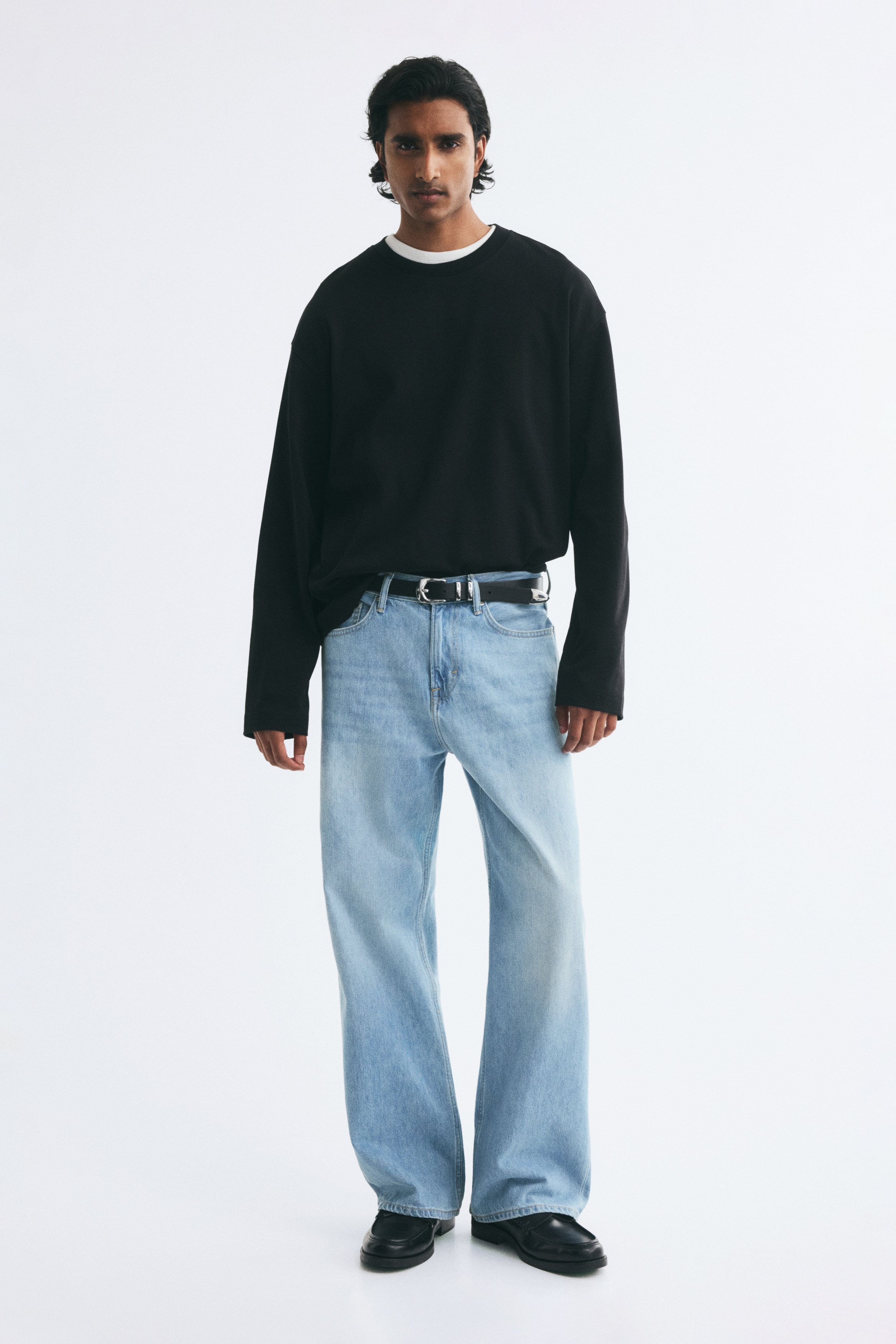 Light blue rigid denim jeans are showcased front-facing, with a regular waist and a button fly. They are crafted in a five-pocket style, featuring a dropped crotch and a straight, loose fit, offering additional space around the entire leg from the seat to the hem.
