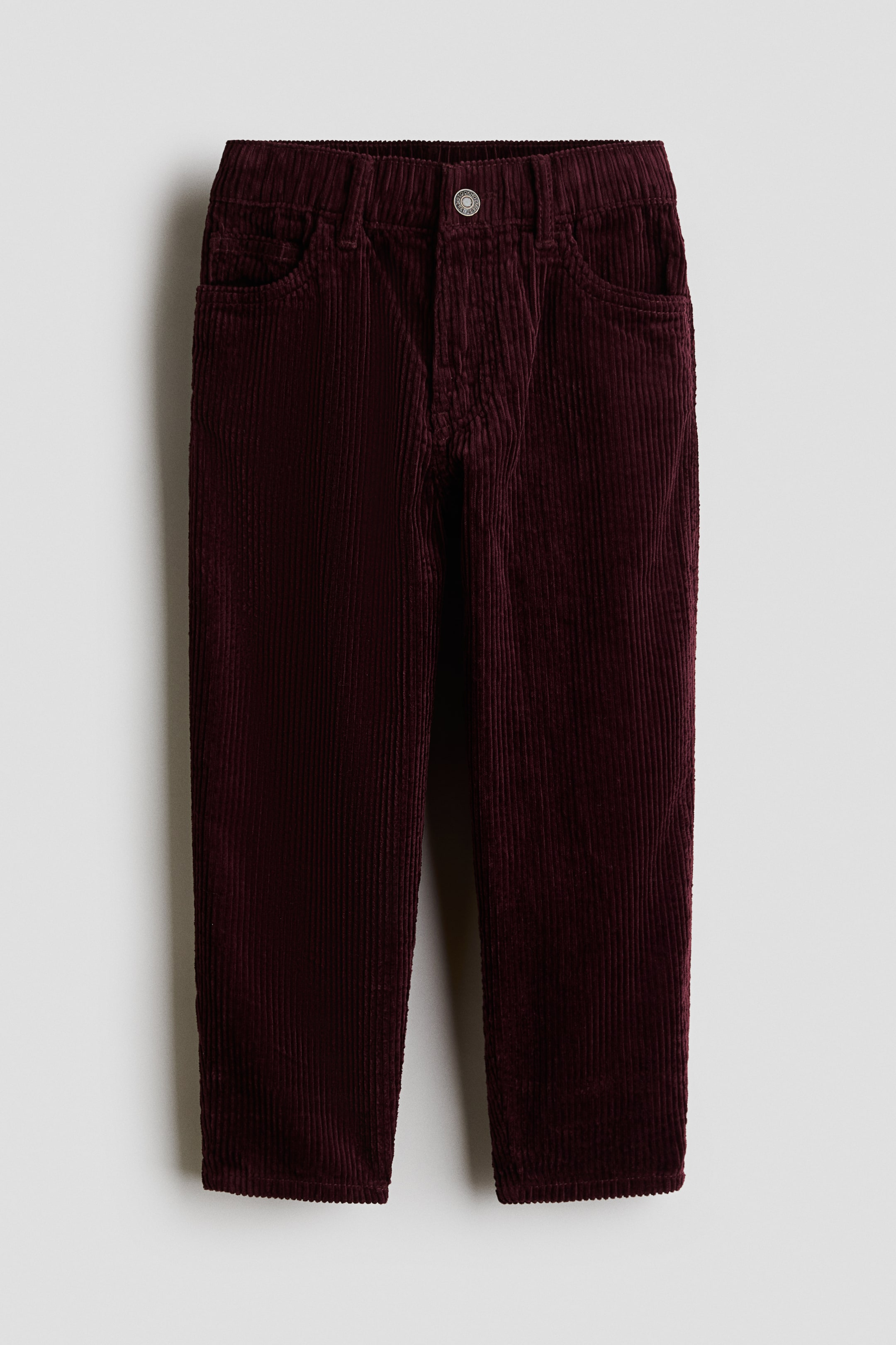 View larger image: A pair of dark burgundy corduroy pants is shown from the front, featuring a loose-fit silhouette with a ribbed texture and a classic five-pocket design. The pants are displaying a waistband with belt loops, an elasticated structure, and a central metal press-stud closure.