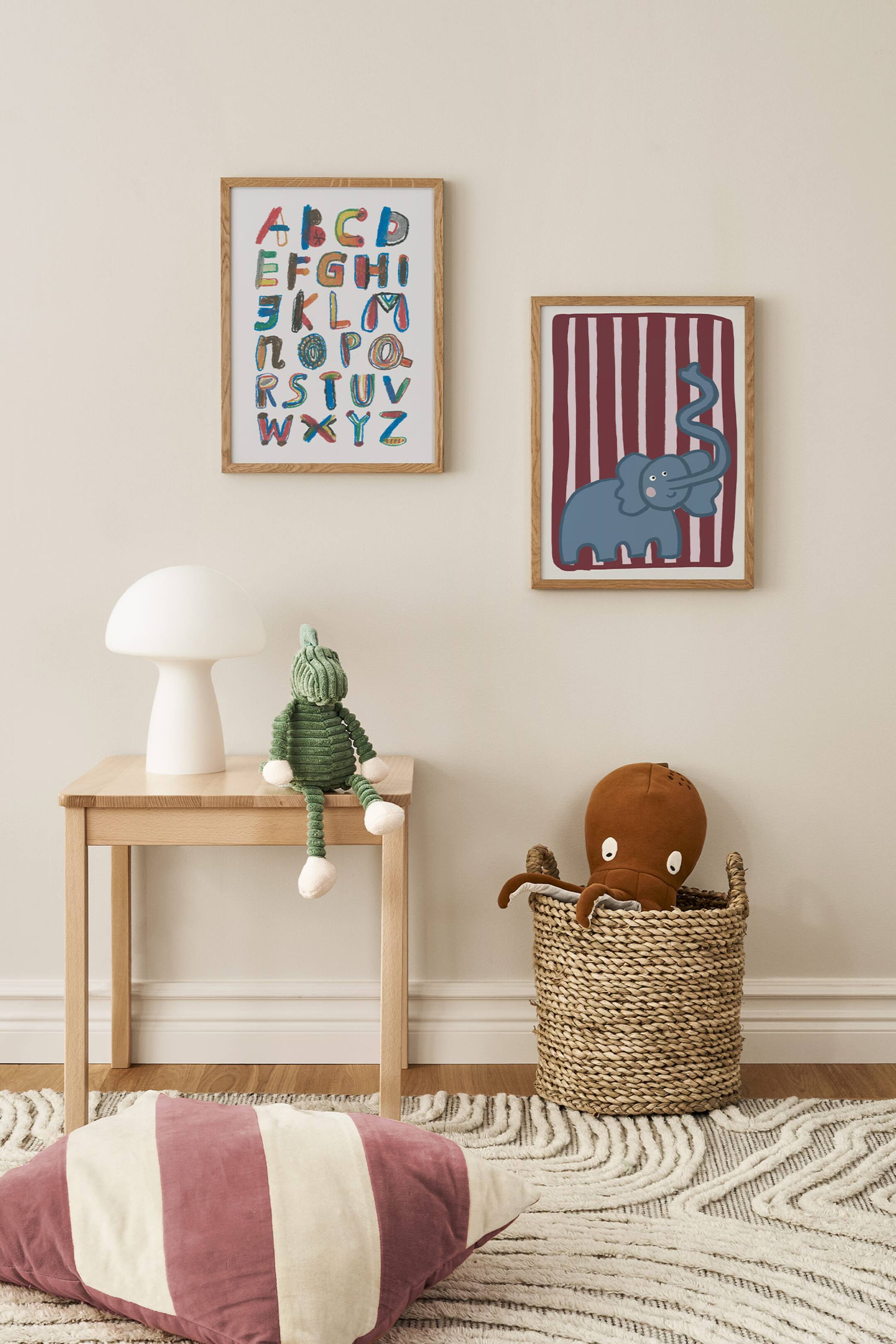 Grotere afbeelding bekijken: Twee rechthoekige kunstprints met een houten lijst hangen aan een neutraalgekleurde muur; de print links toont een kleurrijk, met de hand getekend alfabet, terwijl de print rechts een blauwe cartoonolifant met opgetilde slurf laat zien tegen een kastanjebruine en wit verticaal gestreepte achtergrond.