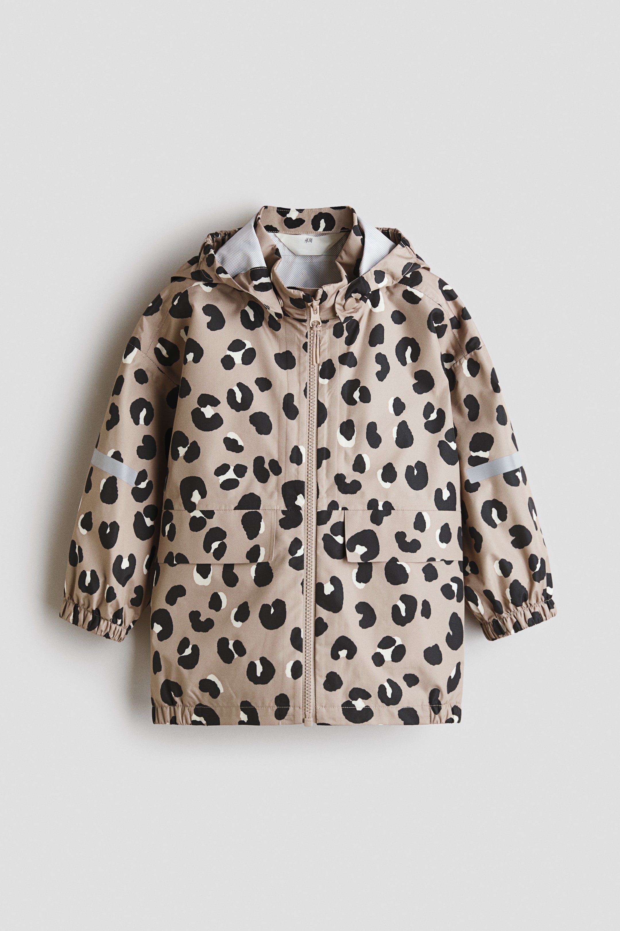 View larger image: The rain jacket is showcased from the front, adorned with a beige and black leopard print. It highlights a detachable hood, a stand-up collar, a central zip closure, and two flap pockets. Additionally, it features elasticated cuffs, an elasticated hem, and reflective details on the sleeves.
