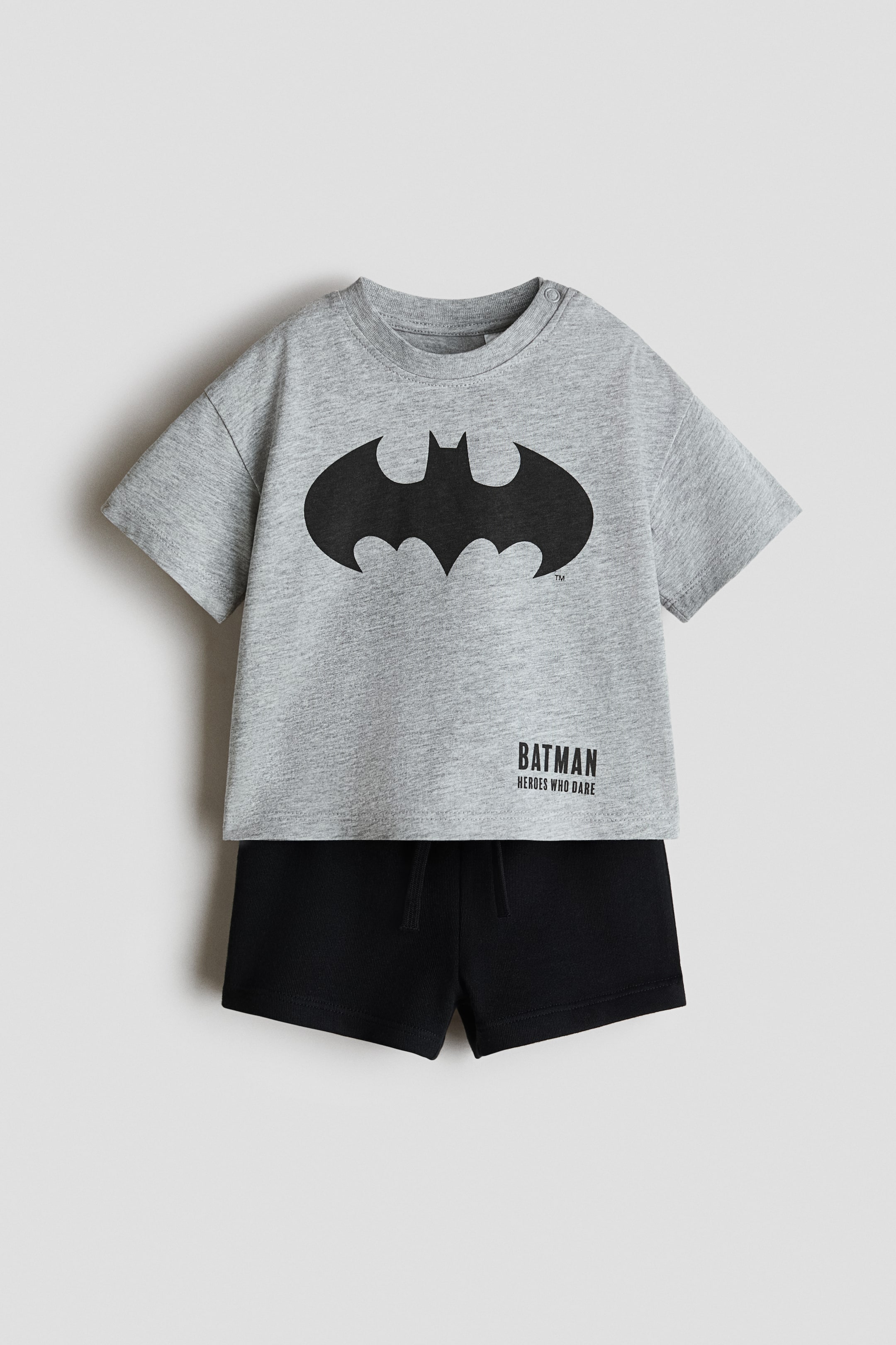View larger image: 2-piece printed set, front-facing. Ang grey marl short-sleeved t-shirt ay may crew neck na may snaps sa isang balikat at isang malaking black Batman logo sa dibdib, kasabay ng "Batman Heroes Who Dare" na teksto. Ang black shorts na may elasticated drawstring waistband ay kumukumpleto sa set.