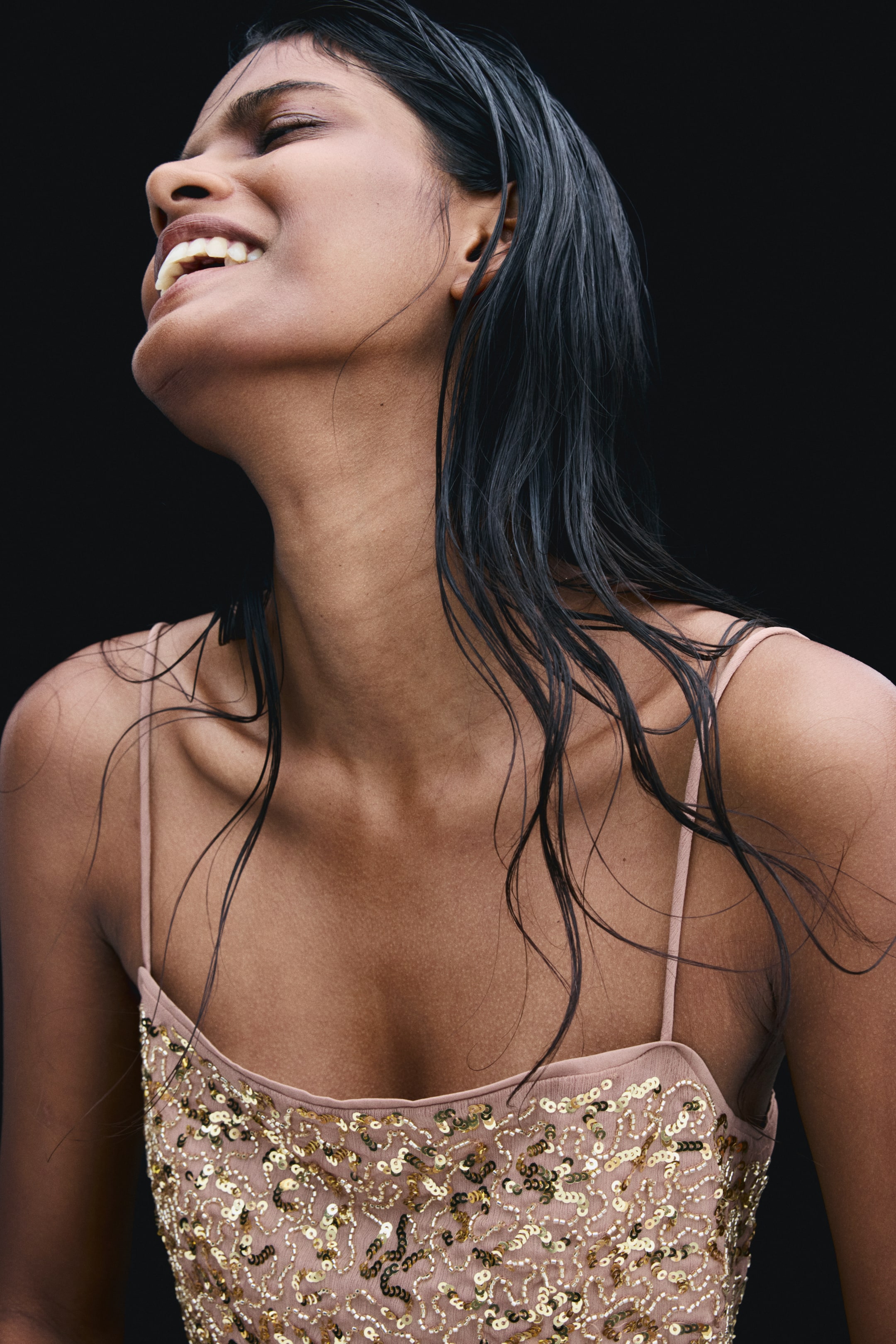 View larger image: A light pink camisole top featuring thin spaghetti straps and gold sequin embellishments is being worn by the model. The top has a scoop neckline and is detailed with shimmering gold-toned sequins stitched onto the fabric.