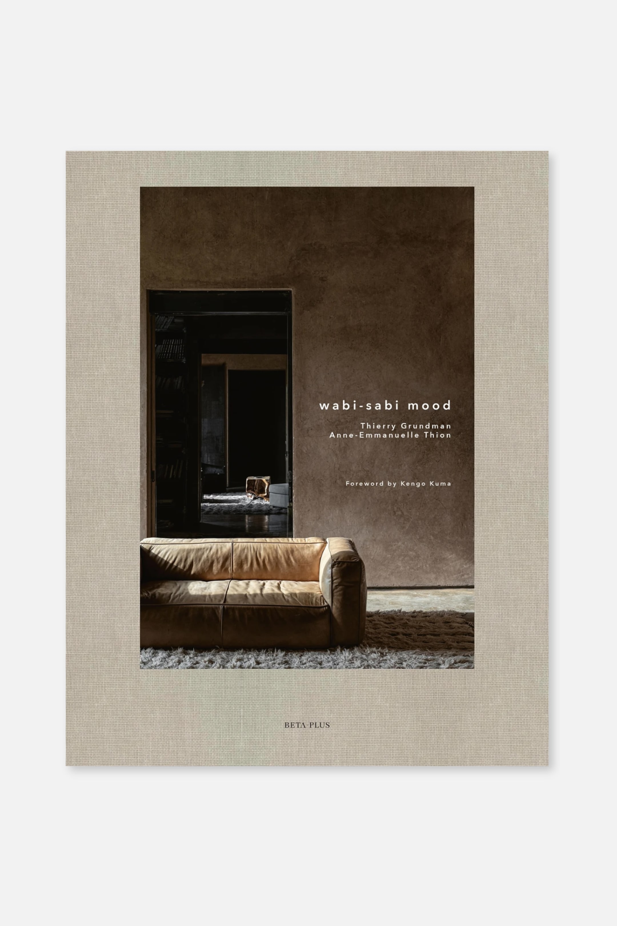 Größeres Bild anzeigen: Ein Hardcover-Buch mit einem hellbeigen, strukturierten Leinen-ähnlichen Einband, das ein zentrales Foto eines Innenraums zeigt. Auf dem Foto ist ein hellbraunes Ledersofa zu sehen, das leicht nach links auf einem flauschigen Teppich steht. Der Titel "wabi-sabi mood" und die Autorennamen sind in Weiß auf dem Bild gedruckt, während "BETA PLUS" am unteren beigen Rand steht.