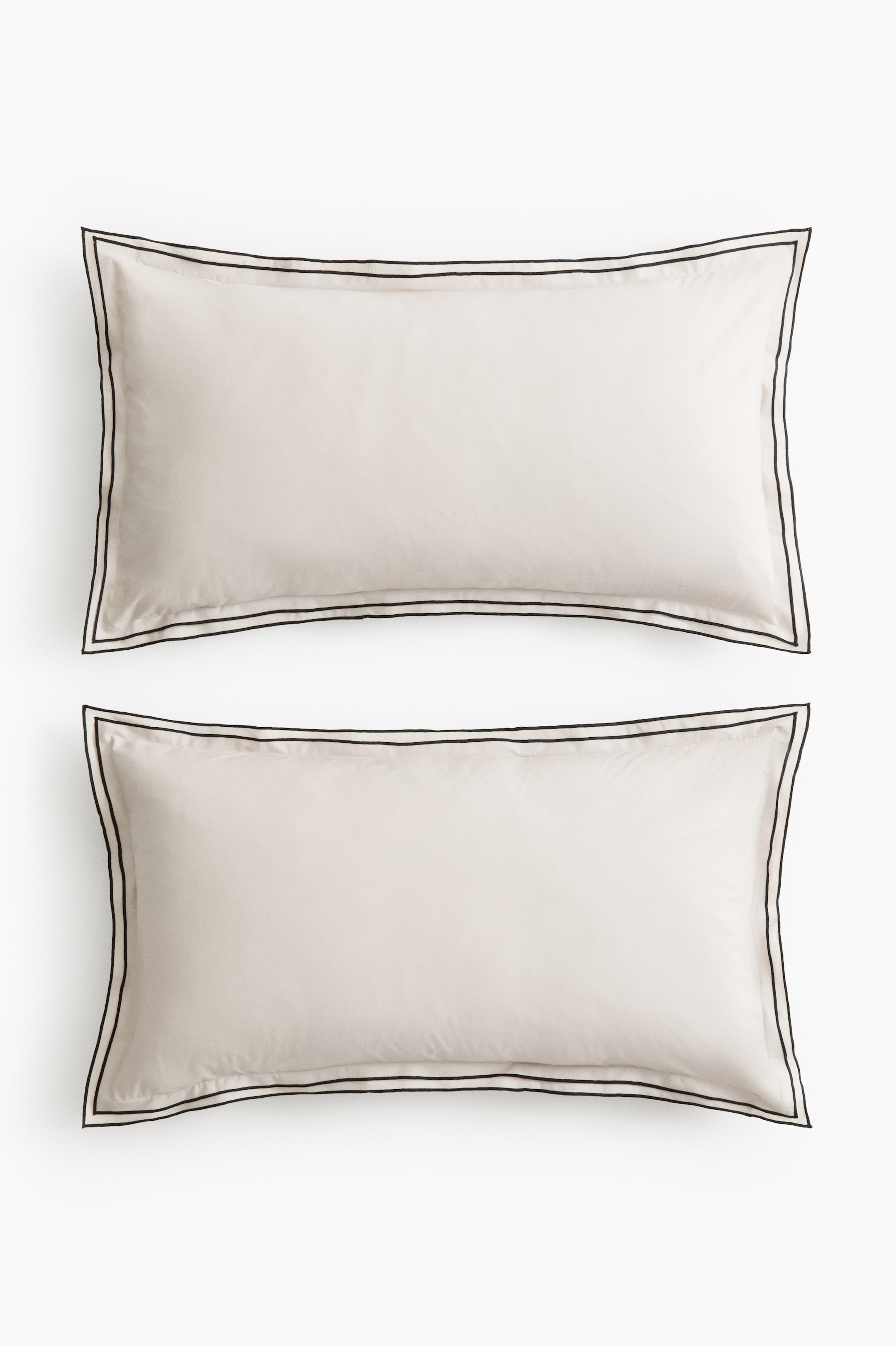 View larger image: Two off-white pillowcases are laid flat, one atop the other, each showcasing a double black stitched border along all four edges.