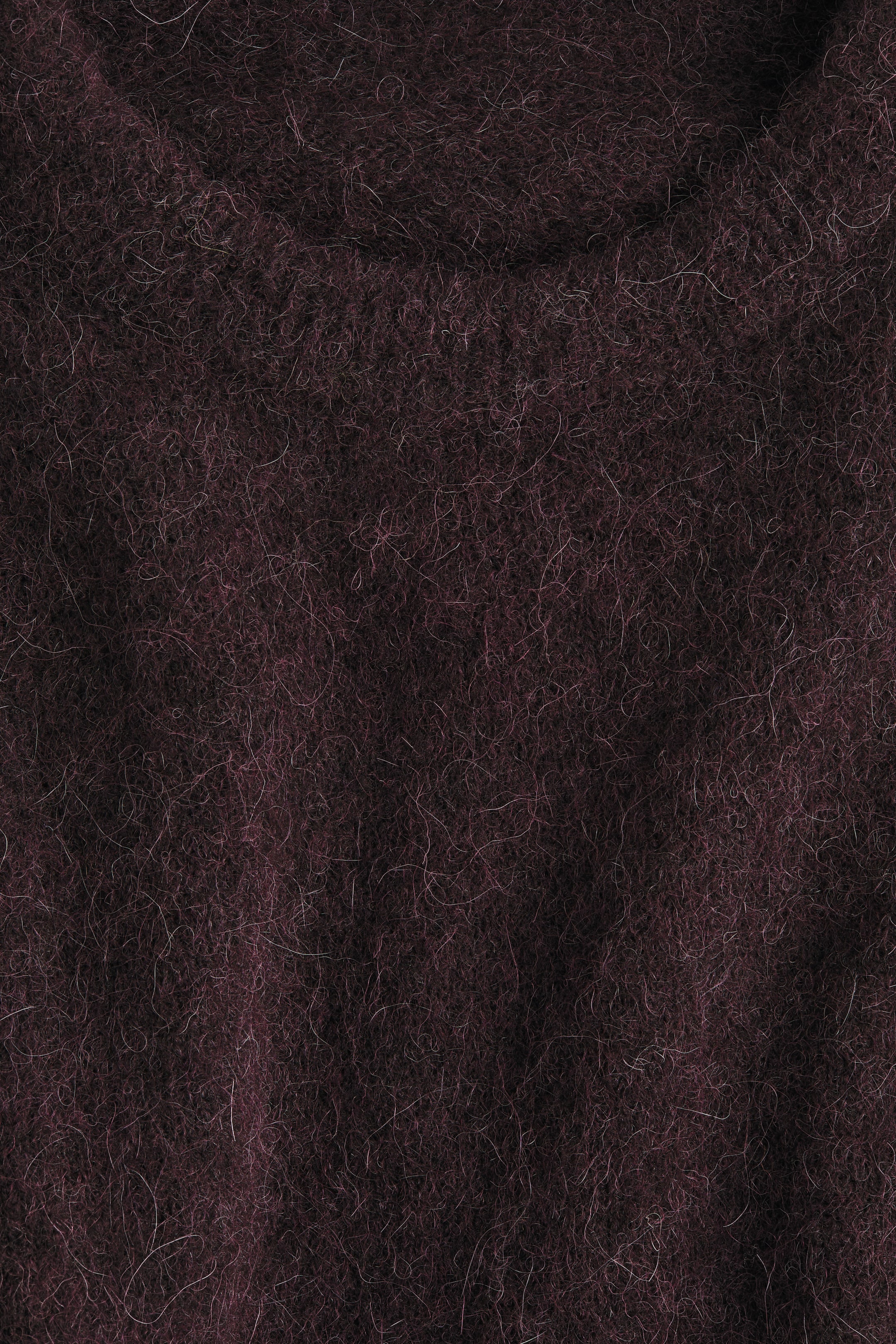 Ampliar la imagen: El suéter de gran tamaño exhibe su textura de punto suave, apareciendo oscuro con fibras más claras visibles, consistente con una mezcla de alpaca y lana.